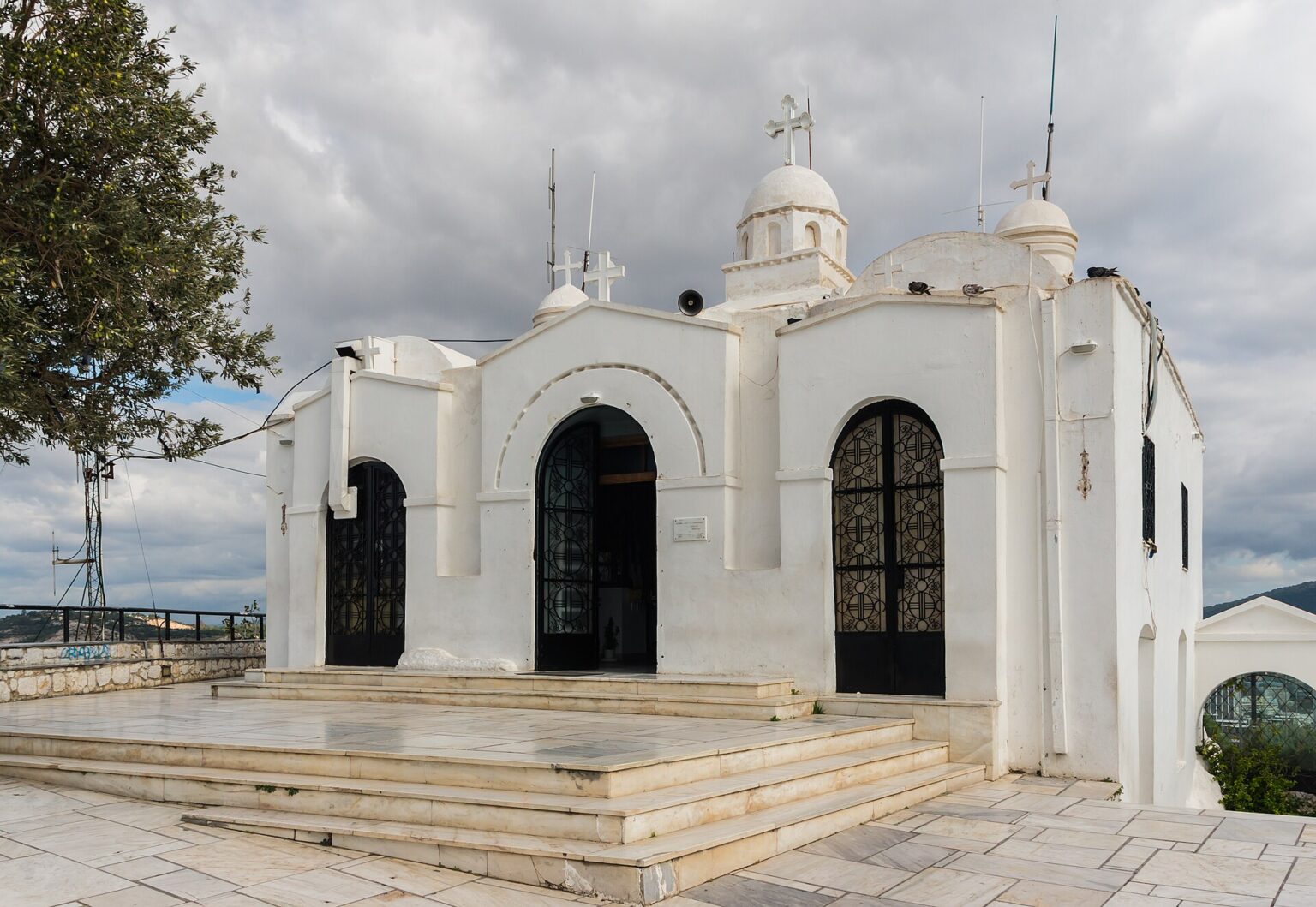 The whitewashed chapel of Agios Georgios on the summit of Lycabettus, with its white domes, its bell tower, its open iron gates and the marble forecourt at the entrance