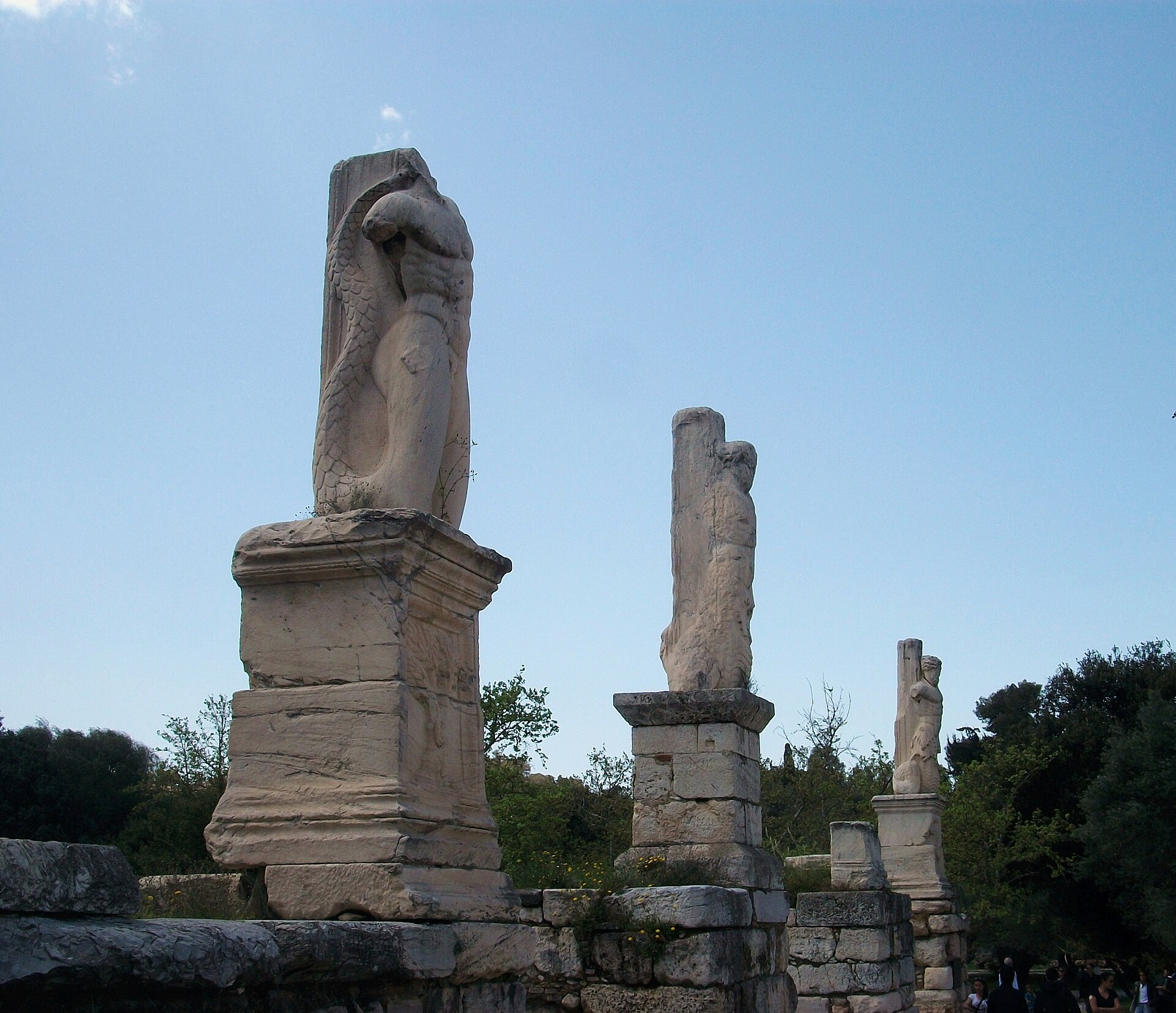3 pillars carved as giants and tritons, remains of the facade of the Odeon of Agrippa, standing on their pedestals against the sky of the Ancient Agora of Athens
