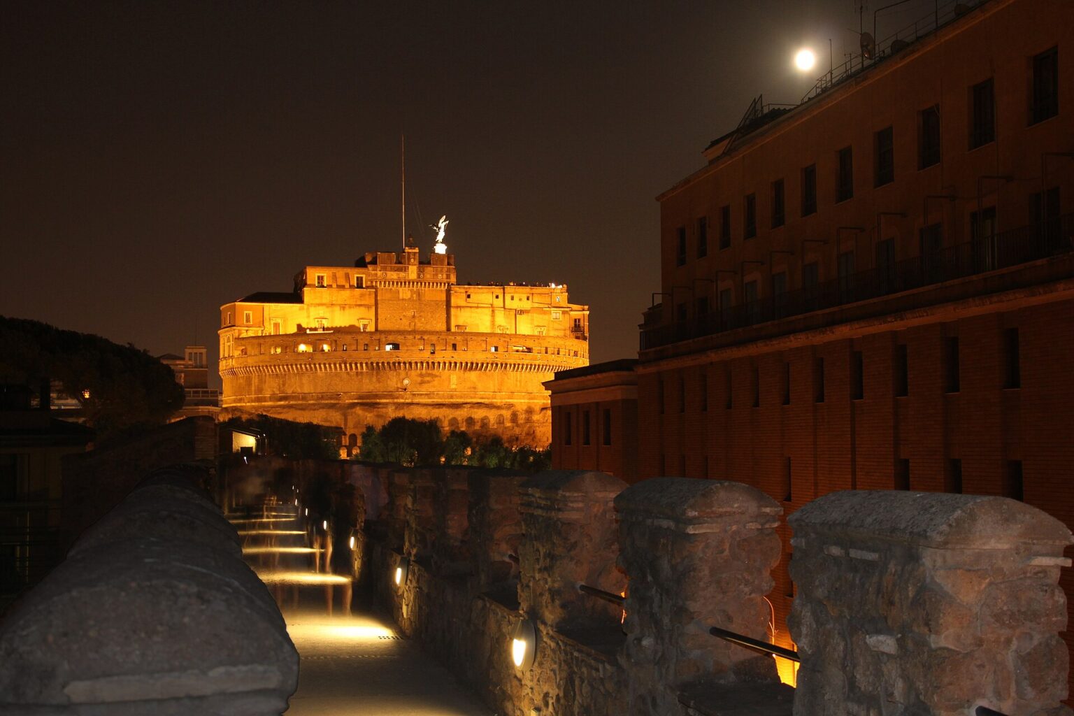 The walkway along the top of the Passetto di Borgo at night, leading towards Castel Sant'Angelo lit up in the distance