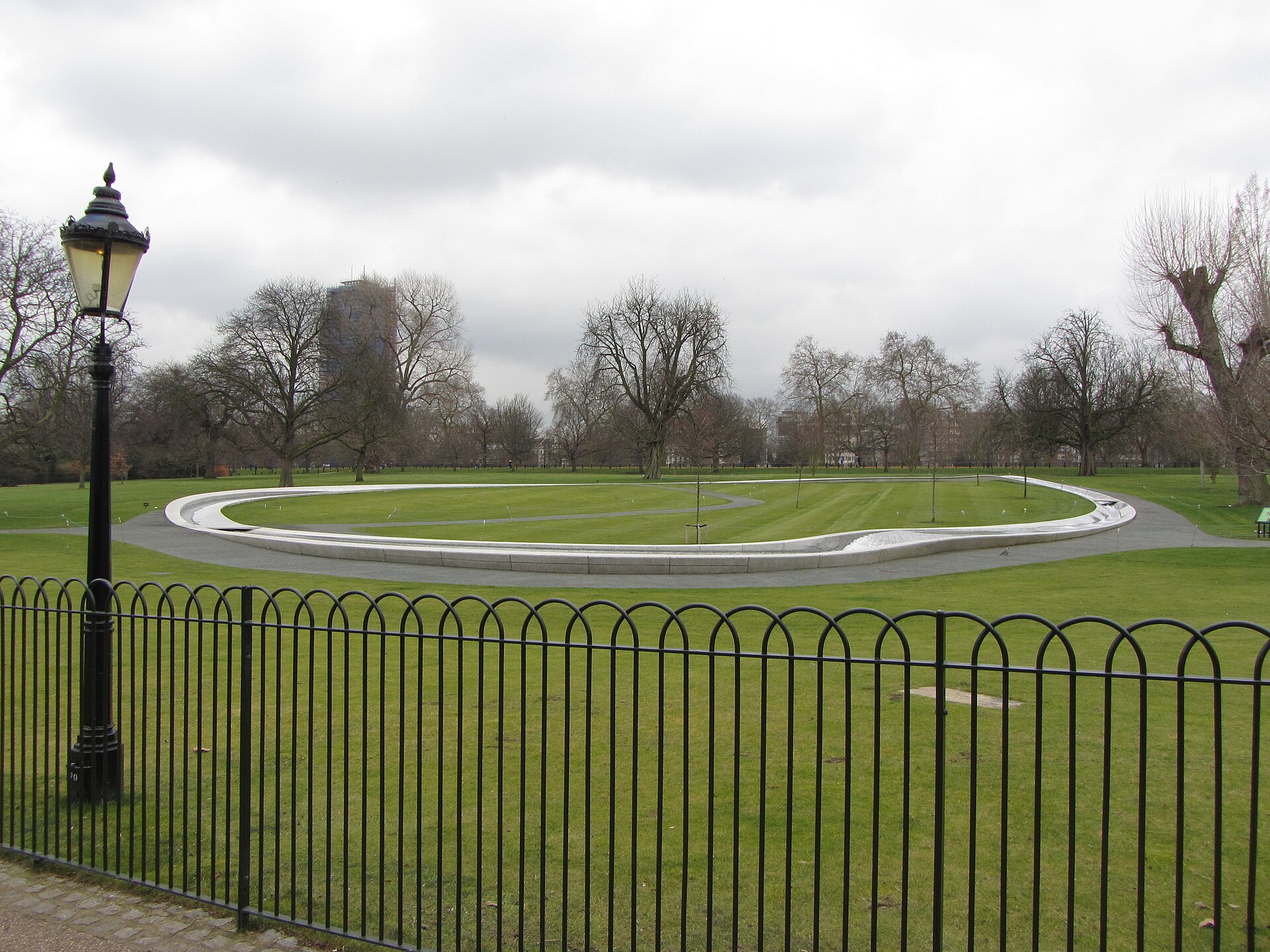 The Diana, Princess of Wales Memorial Fountain in Hyde Park: an oval ring of pale granite set in the lawn, behind low railings and a lamp post
