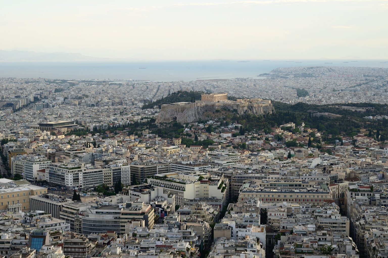 View over Athens from the summit of Lycabettus Hill: the white rooftops of the city centre, the rock of the Acropolis with the Parthenon on top and the coast of the Saronic Gulf in the distance