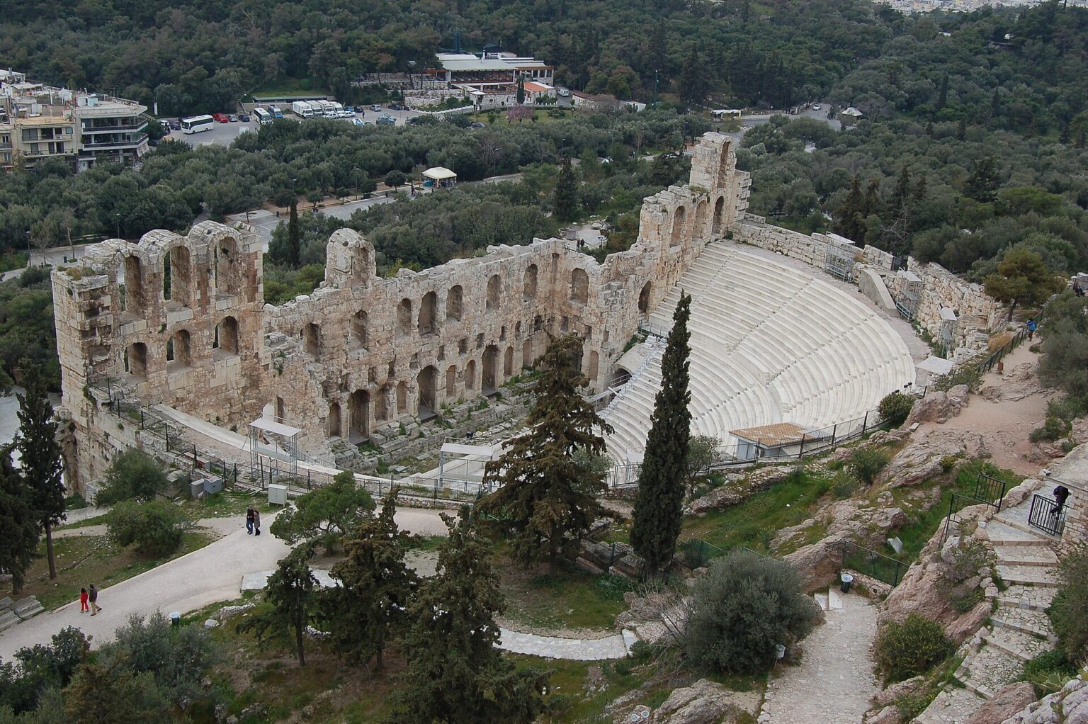 The Odeon of Herodes Atticus seen from above: the semicircular white marble auditorium set into the slope below the Acropolis, closed at the front by the two-storey arcaded stage wall