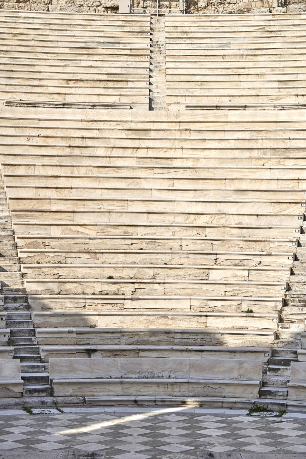 Restored marble rows of one wedge of seating in the Odeon of Herodes Atticus, with the seat numbers painted row by row, running down to the paved floor of the orchestra