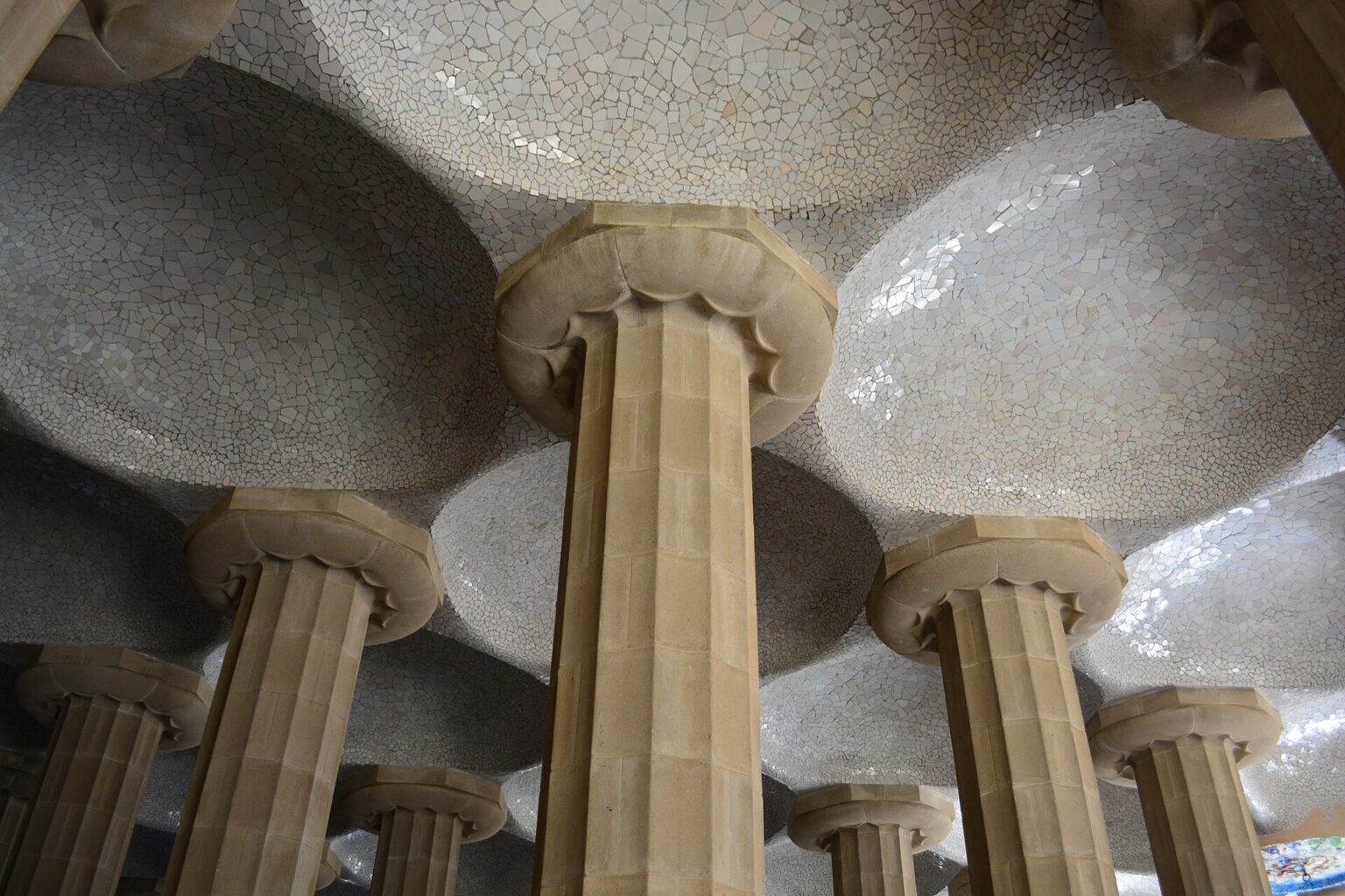 Ceiling of the Hypostyle Room in Park Güell: stone columns with Doric capitals holding up shallow white domes covered in broken tile mosaic
