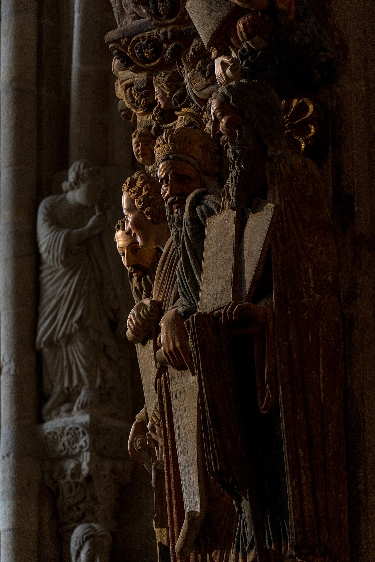 Close-up of the Portico of Glory: granite column statues with traces of red and gold paint, in the half-light of the cathedral's west entrance