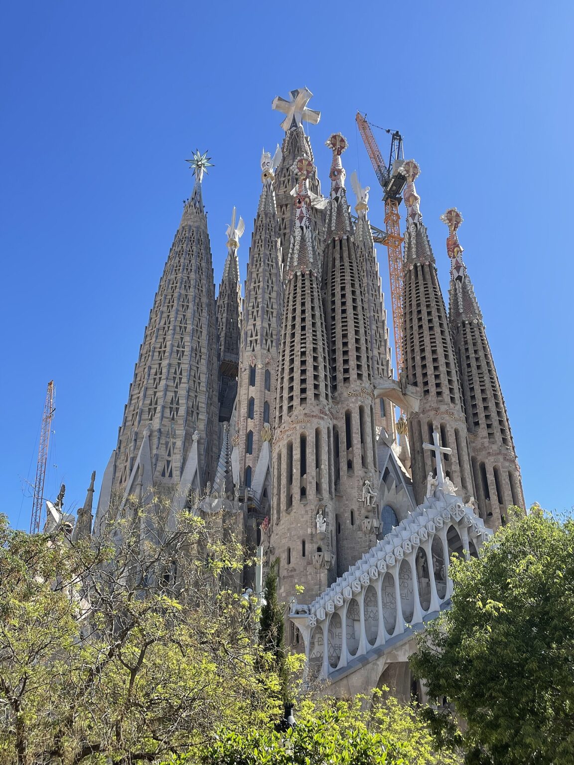 Towers of the Sagrada Familia against a blue sky: the central tower of Jesus Christ topped by a white cross, the star of the tower of the Virgin Mary to its left and, below, the pale pediment of the Passion façade with its white cross