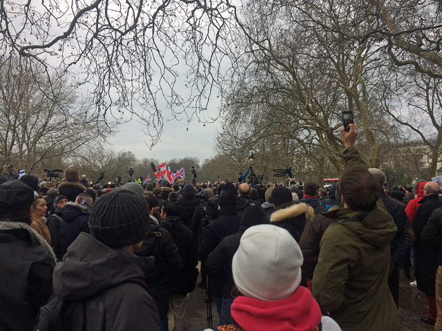 A crowd in winter coats listening to a speaker at Speakers' Corner in the north-east corner of Hyde Park, among bare trees