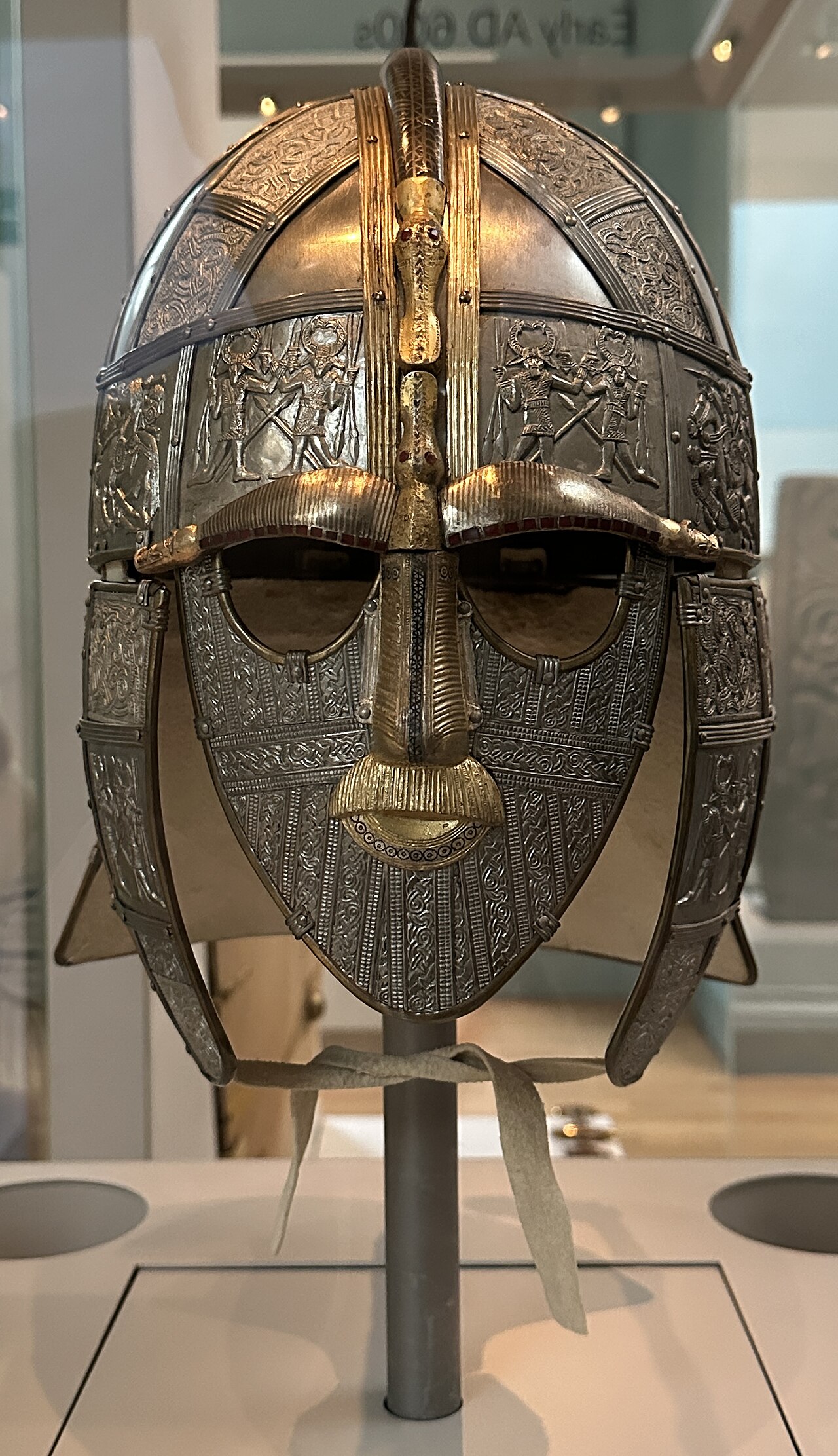 The replica of the Sutton Hoo helmet in its case in Room 41 of the British Museum: an iron helmet with a full face mask, gilded eyebrows and nose, a moustache and panels showing warriors