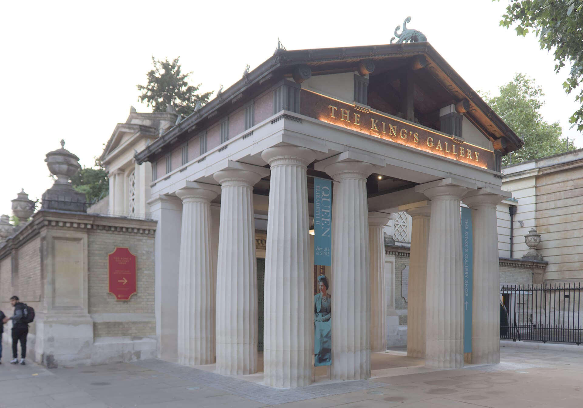 The entrance portico of The King's Gallery, with fluted columns, gilded lettering and a banner for the exhibition Queen Elizabeth II: Her Life in Style