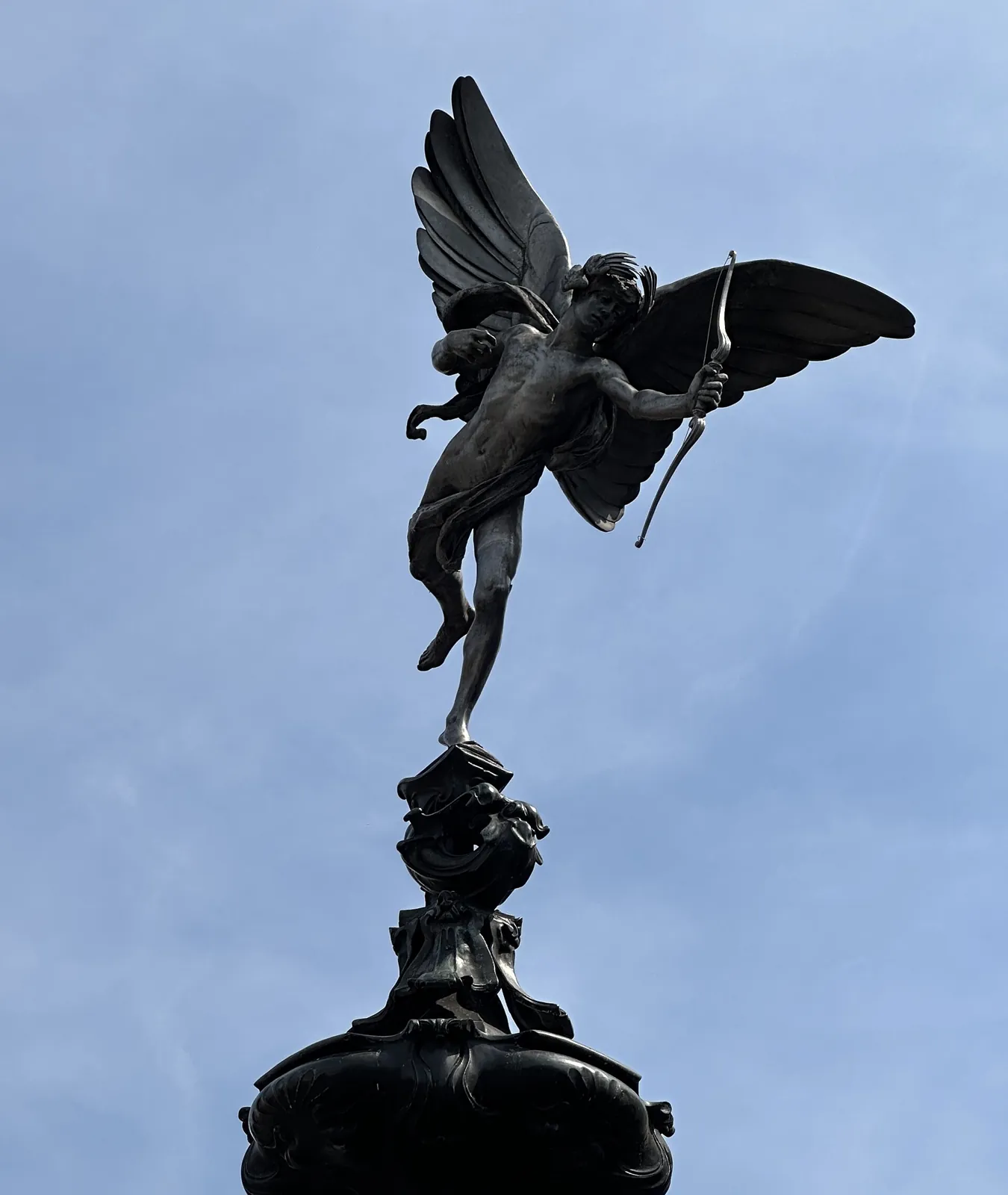 Winged statue of Anteros holding his bow on top of the fountain, against the sky
