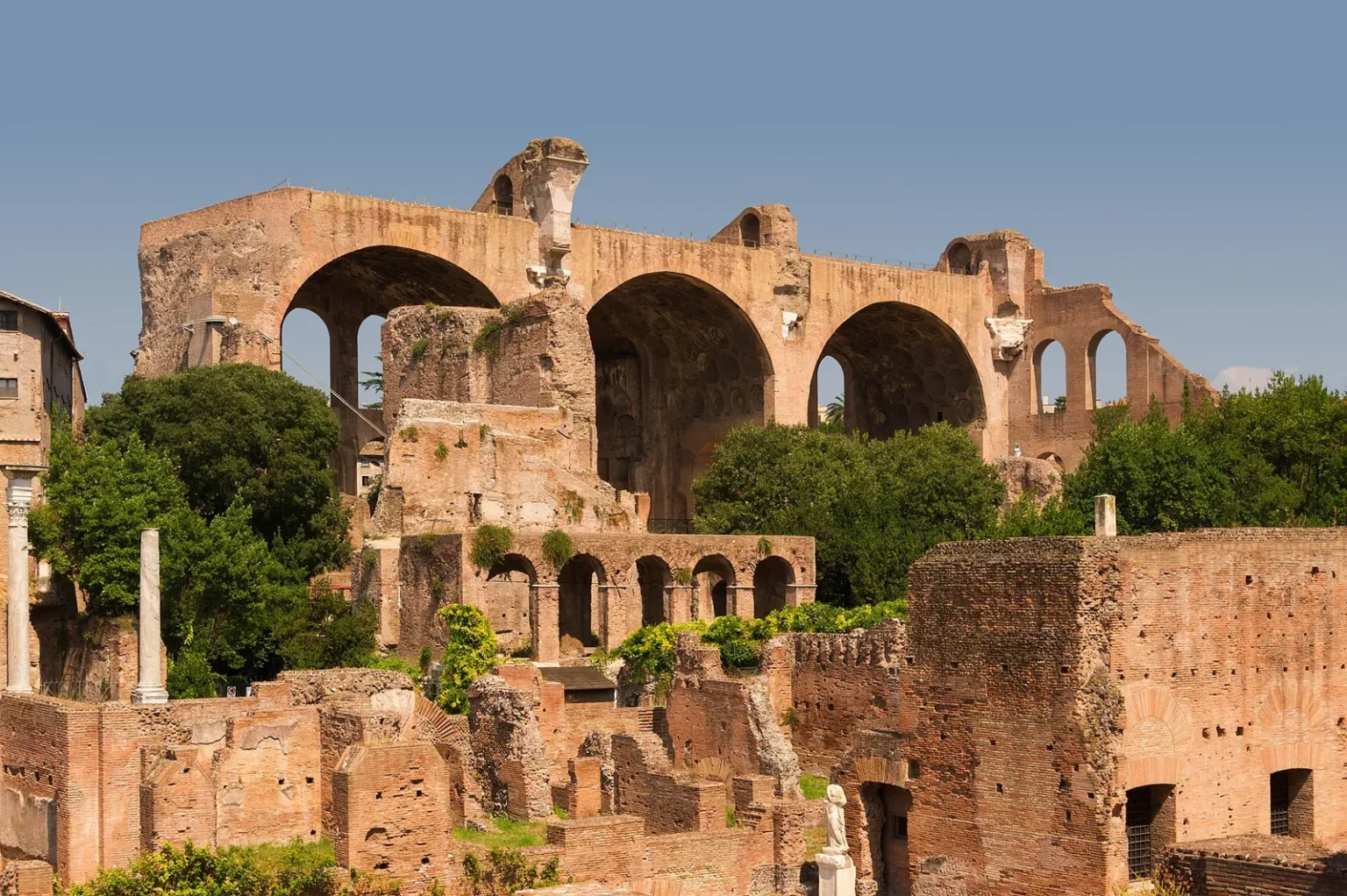 The 3 huge brick vaults that survive of the Basilica of Maxentius, standing above lower brick ruins and green trees in the Roman Forum