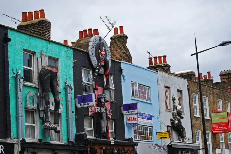 Painted shop fronts on Camden High Street with giant figures above the shops: a pair of legs in boots, a woman and a gorilla