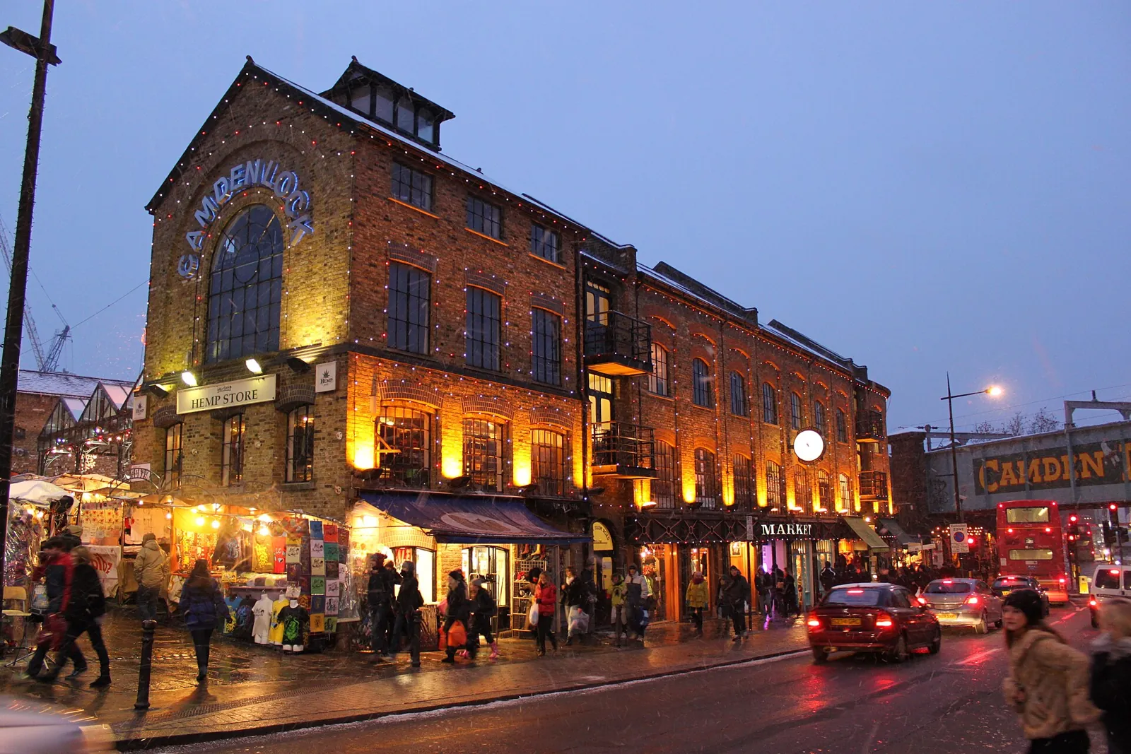 Brick Market Hall building at Camden Lock lit up at dusk, with shops on the ground floor