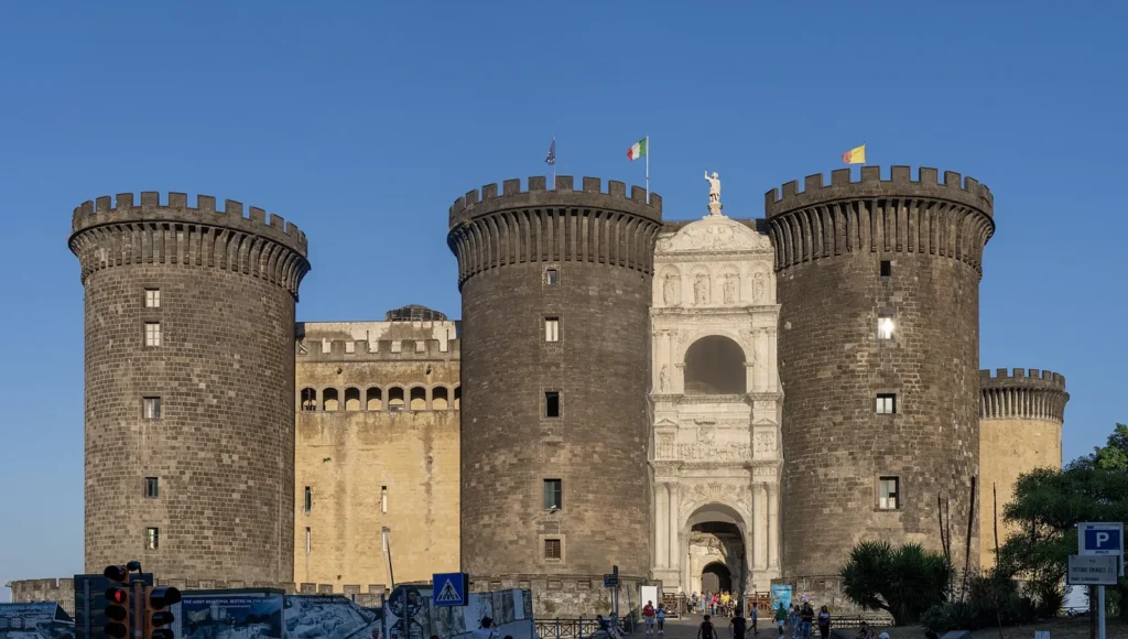 Castel Nuovo in Naples seen from Piazza Municipio: 3 round towers of dark stone with battlements and, between the 2 on the right, the white marble triumphal arch at the entrance