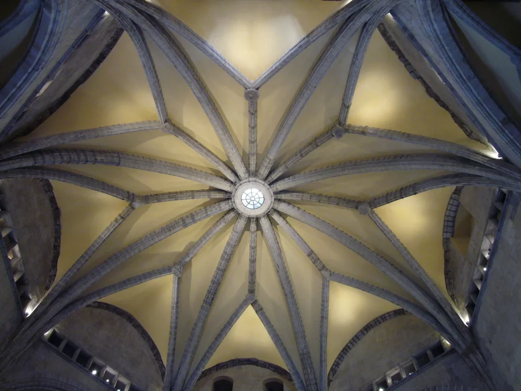 The vault of the Hall of the Barons seen from below: grey stone ribs spreading like a star from a round opening at the centre over pale yellow panels