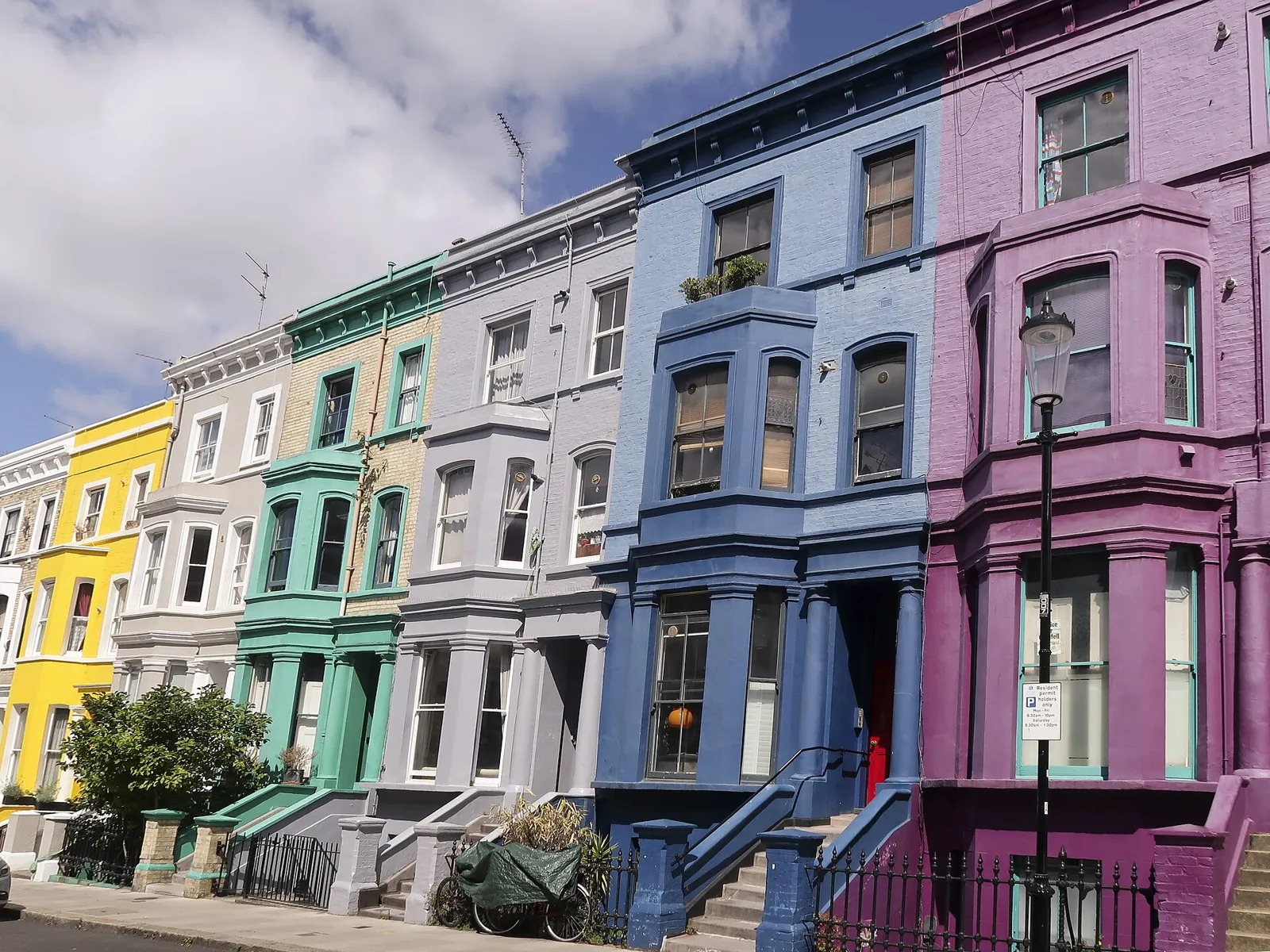 Victorian terraced houses on Lancaster Road painted yellow, green, grey, blue and purple, with bay windows and a black lamp post