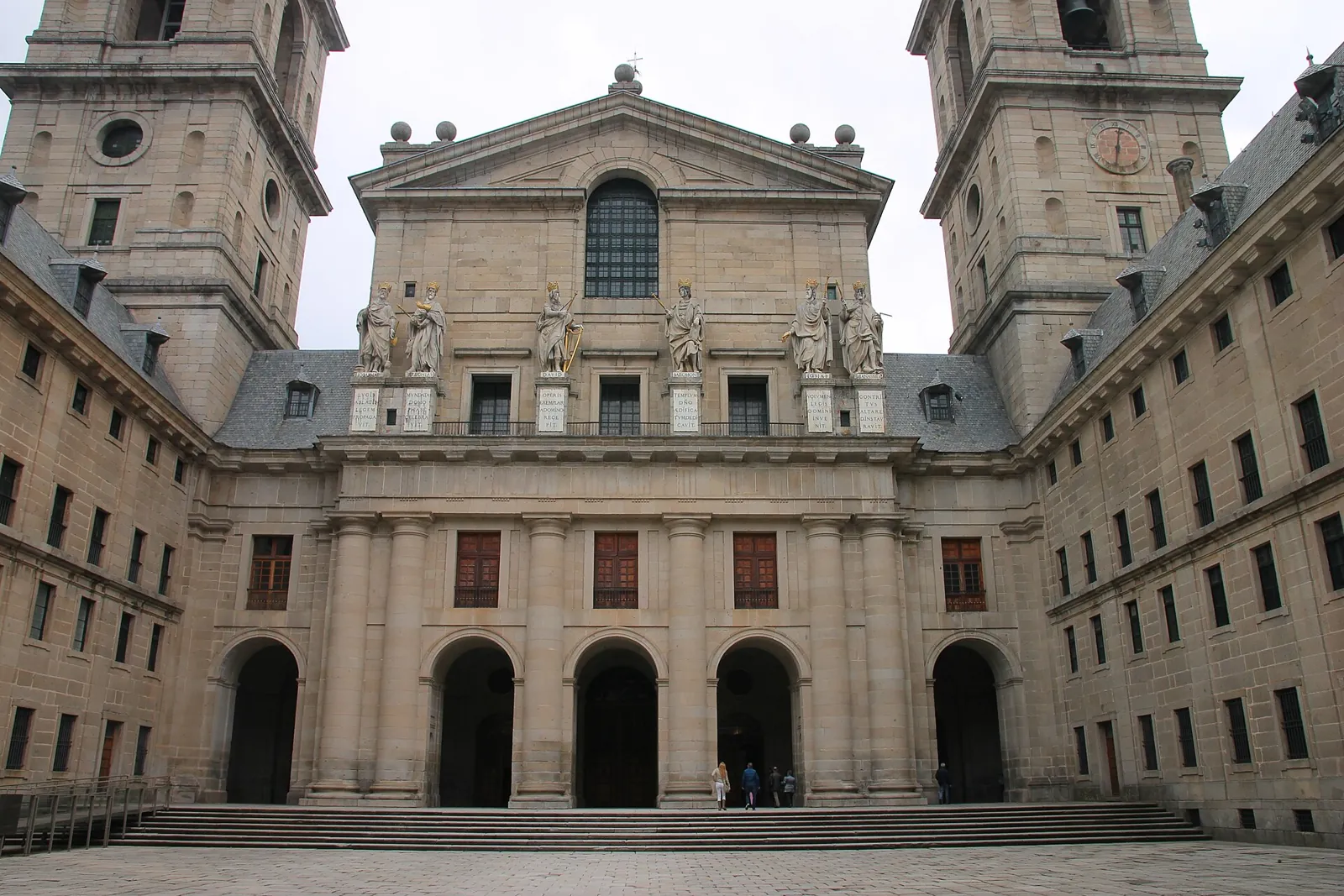 Courtyard of the Kings at El Escorial: the basilica facade with its two towers, pediment and royal statues, framed by the granite walls of the courtyard