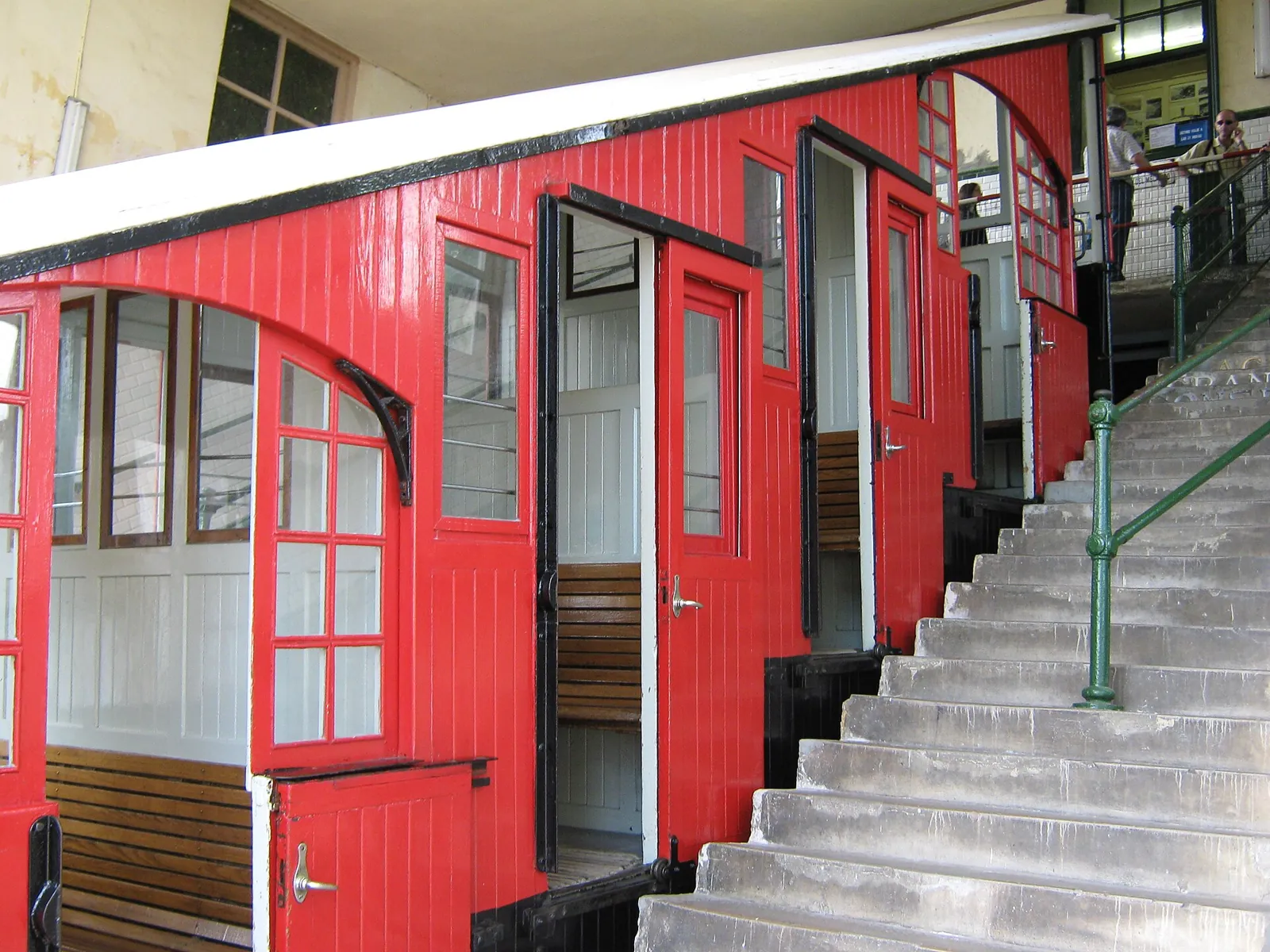Red wooden car of the Igueldo funicular at the top station, with its stepped compartments and the platform stairs beside it