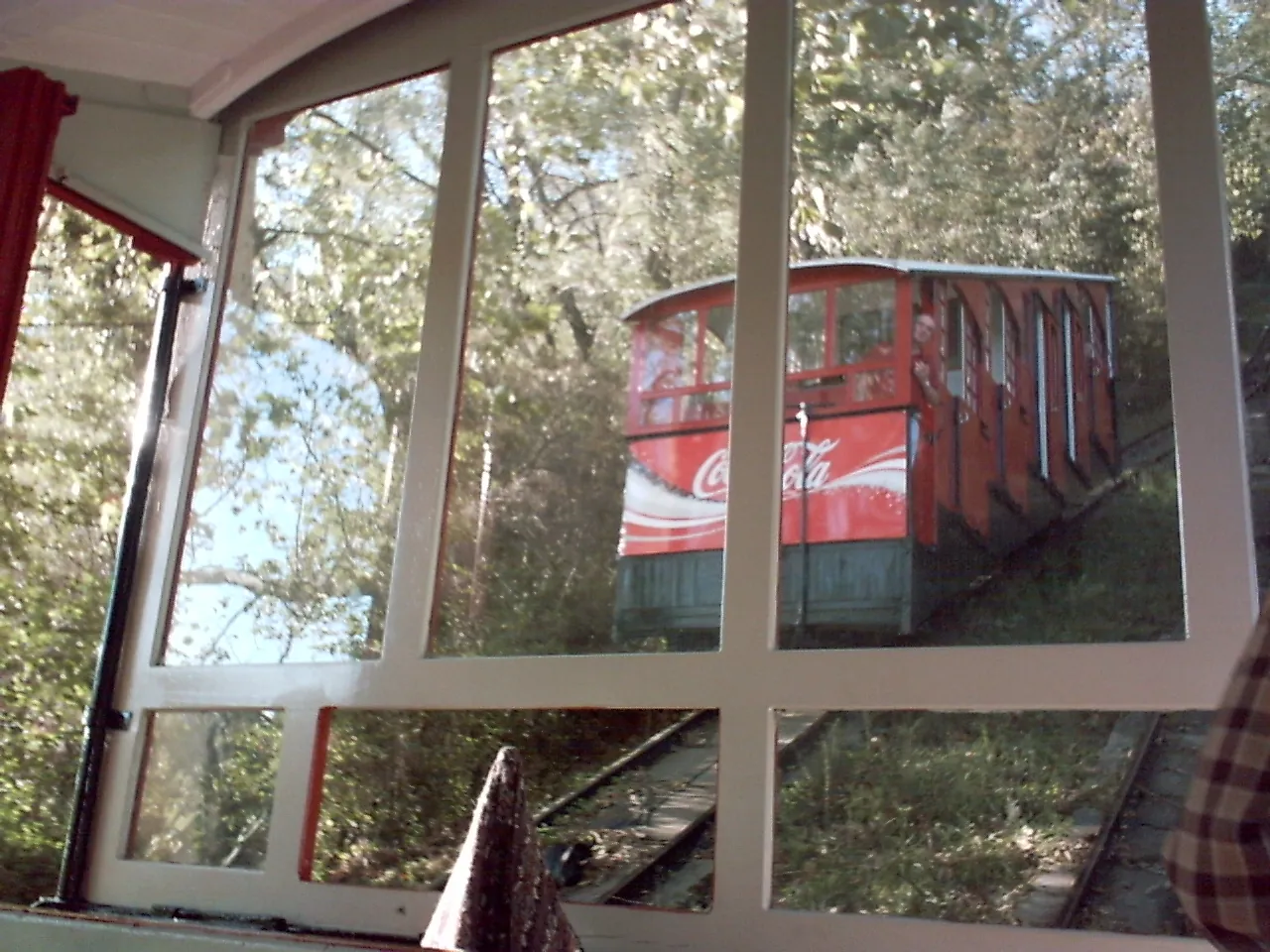 The other Igueldo funicular car seen through the window of a car, among trees, as the 2 cars pass halfway up