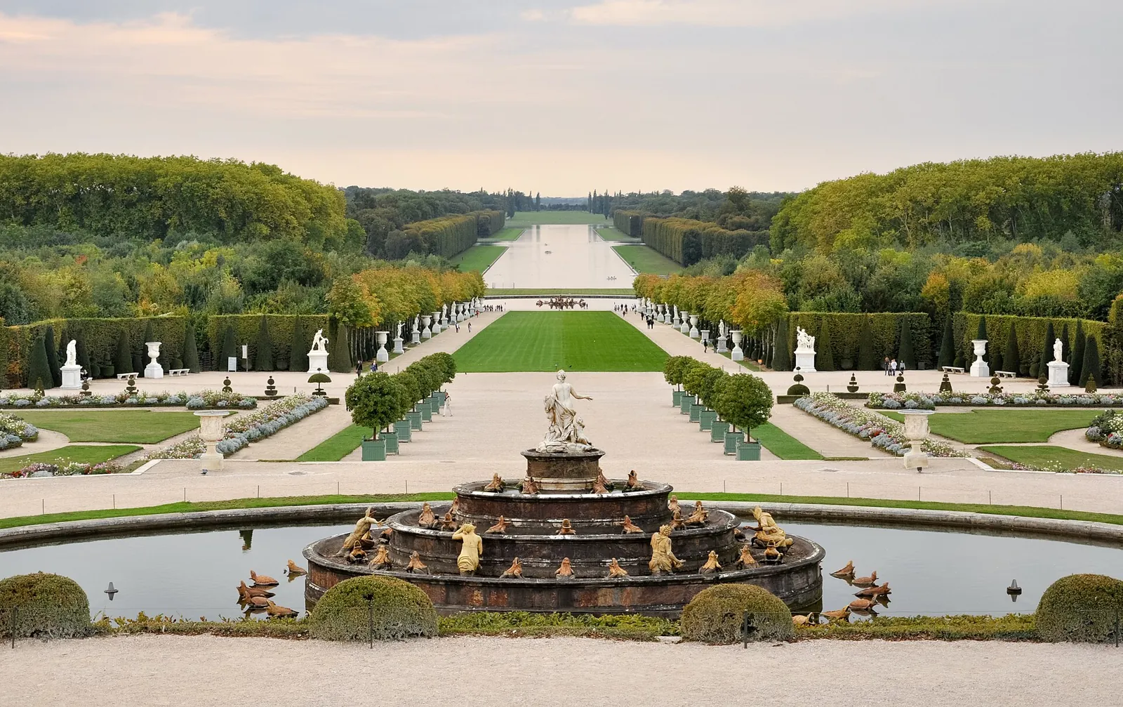 The gardens of Versailles from the terrace: a sculpted fountain in front, parterres and statues, and the Grand Canal between the woods in the distance