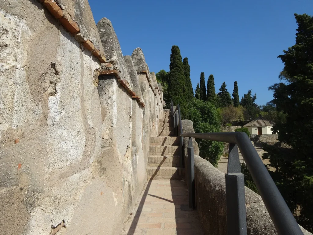 Narrow paved wall walk with steps and a metal handrail beside the battlements of Gibralfaro Castle