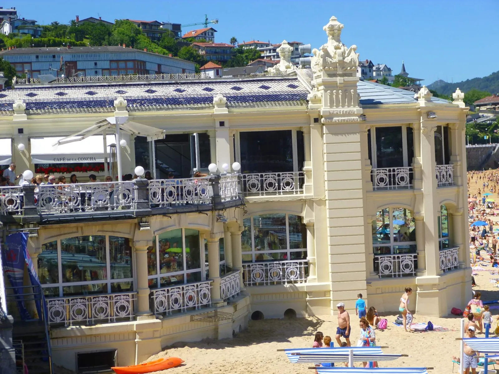 The cream-coloured La Perla building, with white iron balconies, standing on the sand of La Concha among bathers