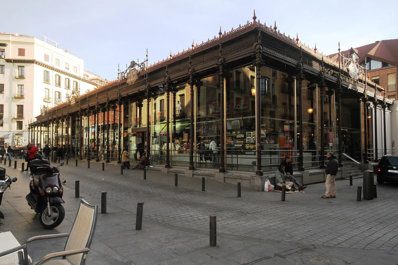 Mercado de San Miguel market hall in Madrid: dark cast-iron columns, glass walls and the ornate roof crest, with the cobbled square in front