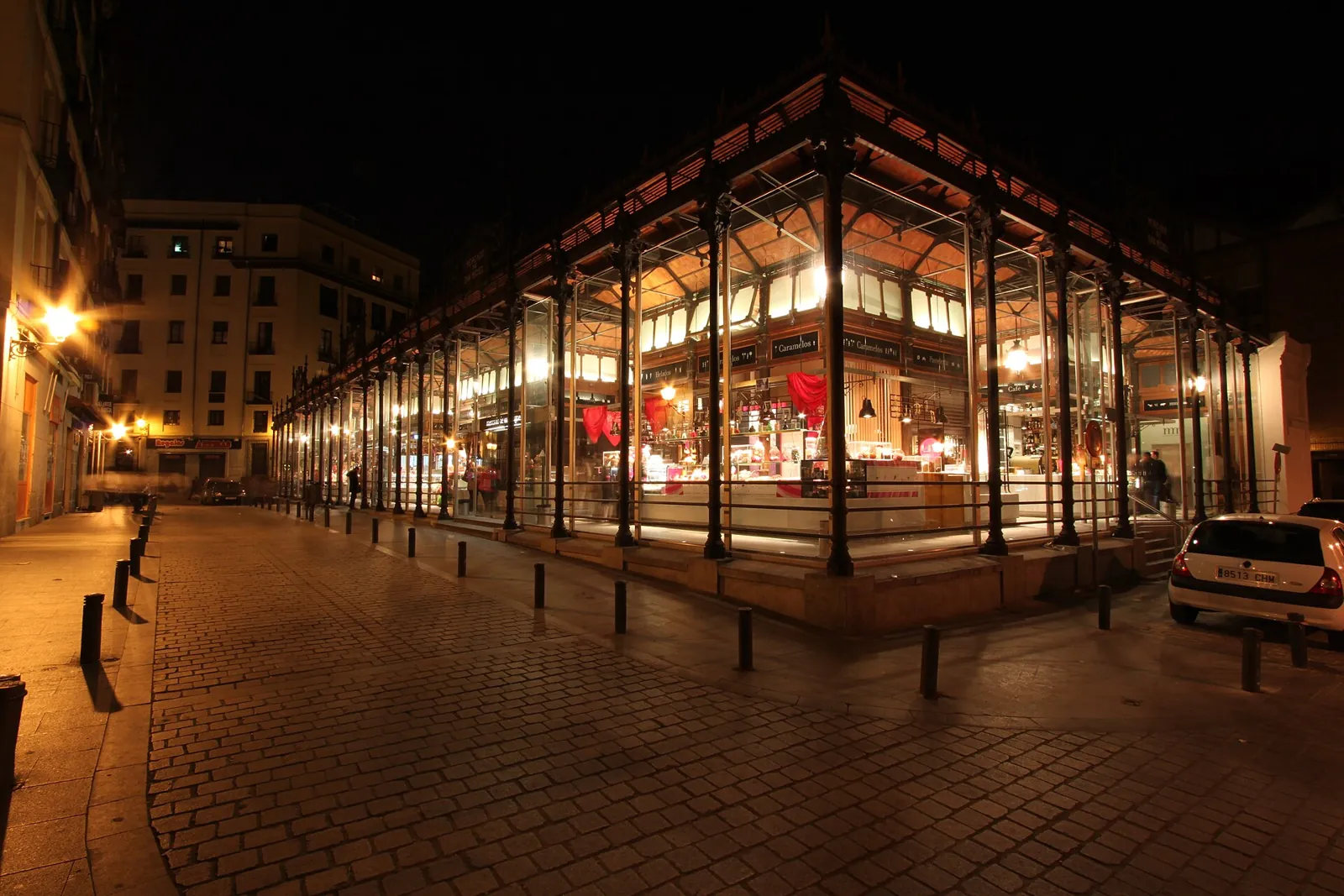 The Mercado de San Miguel at night, its interior lit up behind the glass walls and the cobbled street almost empty