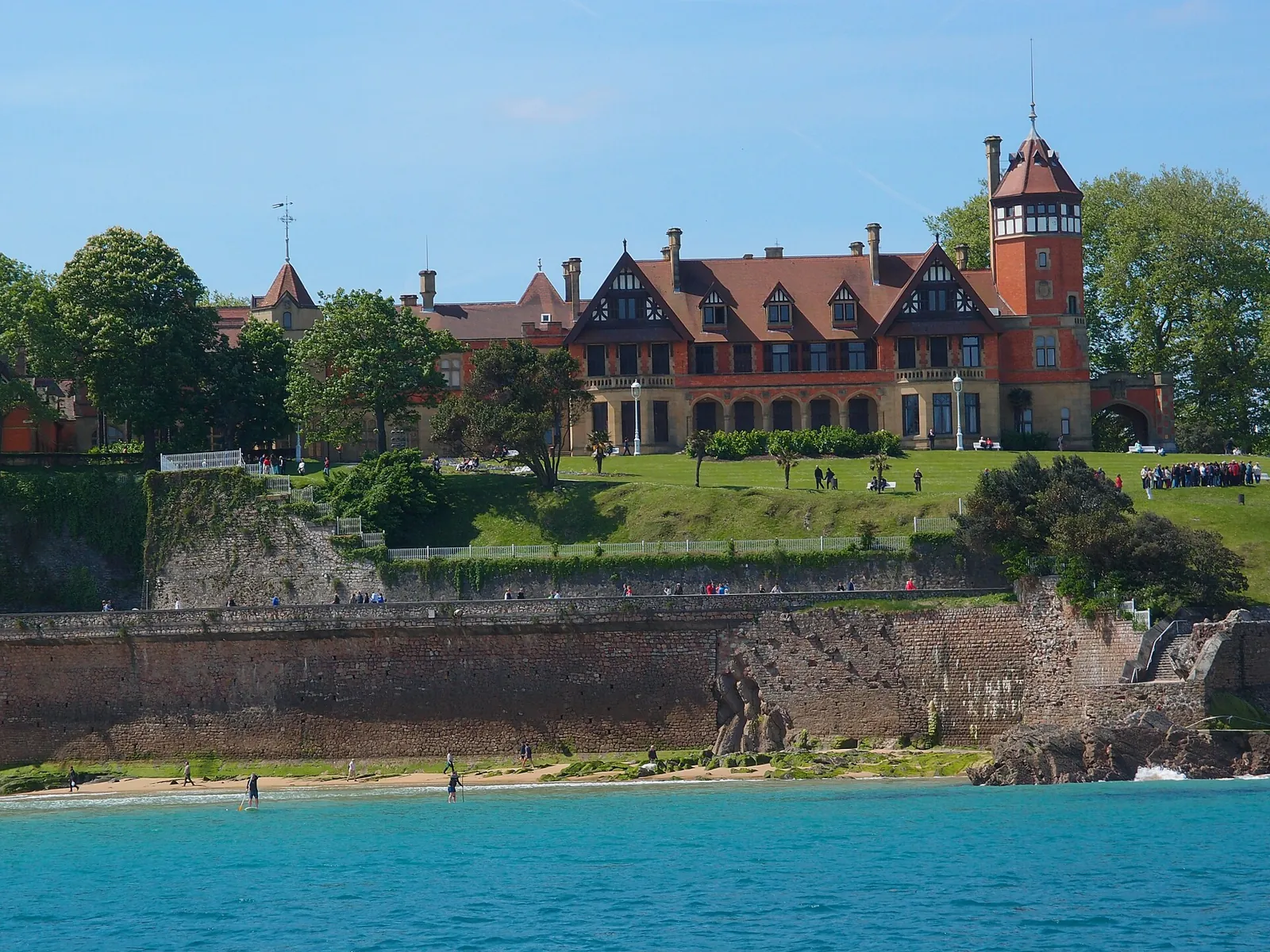 Miramar Palace, in red brick with gabled roofs and a tower, above the gardens and stone wall of the Pico del Loro, by the sea