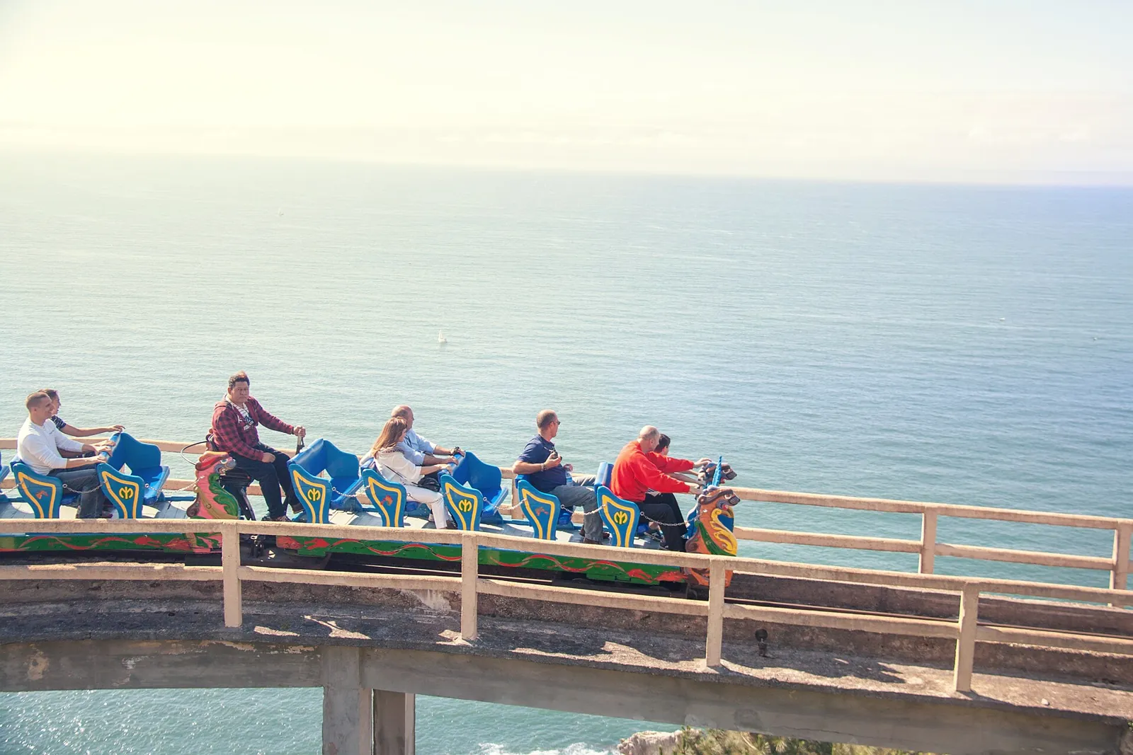 Cars of the Montaña Suiza on Monte Igueldo with riders on a raised section with a railing, and the Bay of Biscay behind