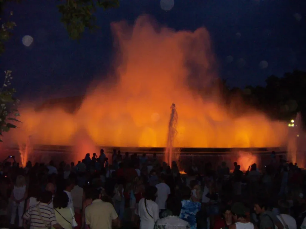 A crowd at night in front of the Magic Fountain of Montjuïc, its jets lit in orange during a show