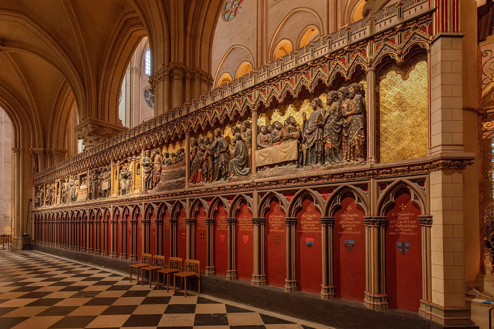 Painted stone reliefs on the choir screen of Notre-Dame, with scenes under Gothic arches above red doors and a chequered floor