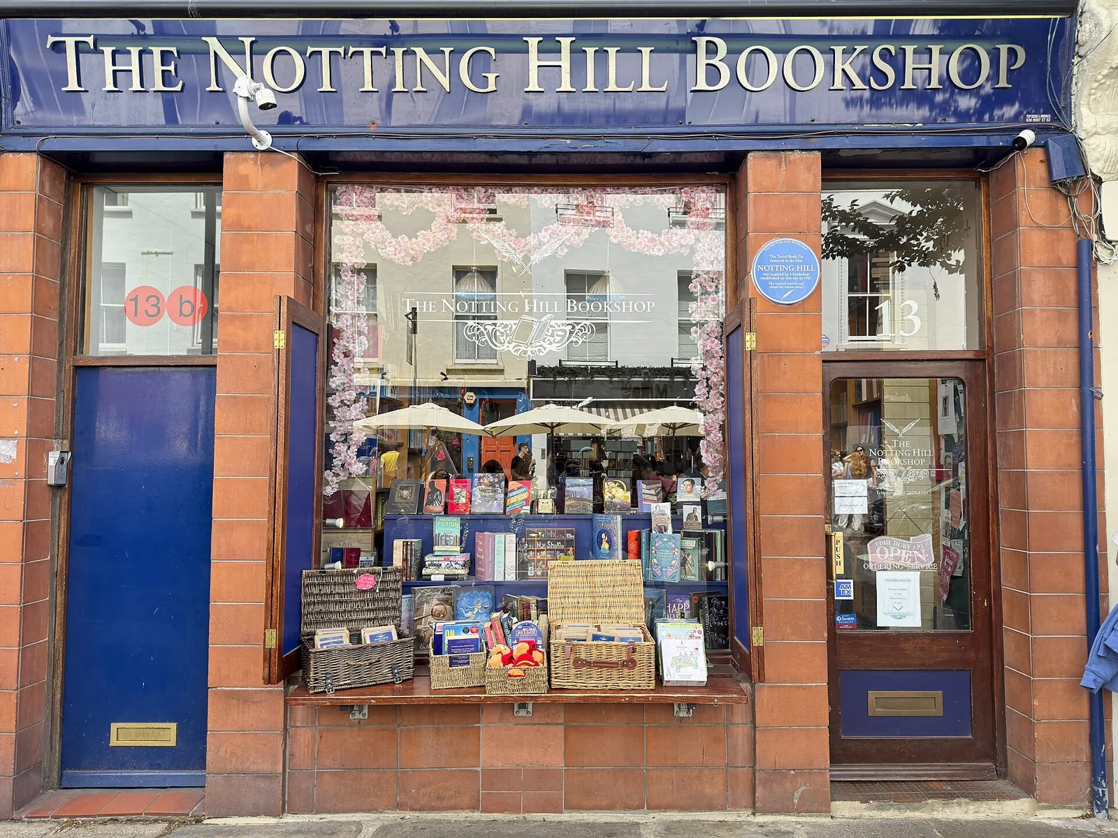 The window of The Notting Hill Bookshop, with its blue sign in gold letters, terracotta tiled pillars and a blue plaque on the front