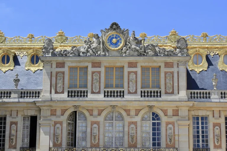 Brick and stone façade of the Marble Courtyard at the Palace of Versailles, with the great gilded clock and sculptures on the slate roof