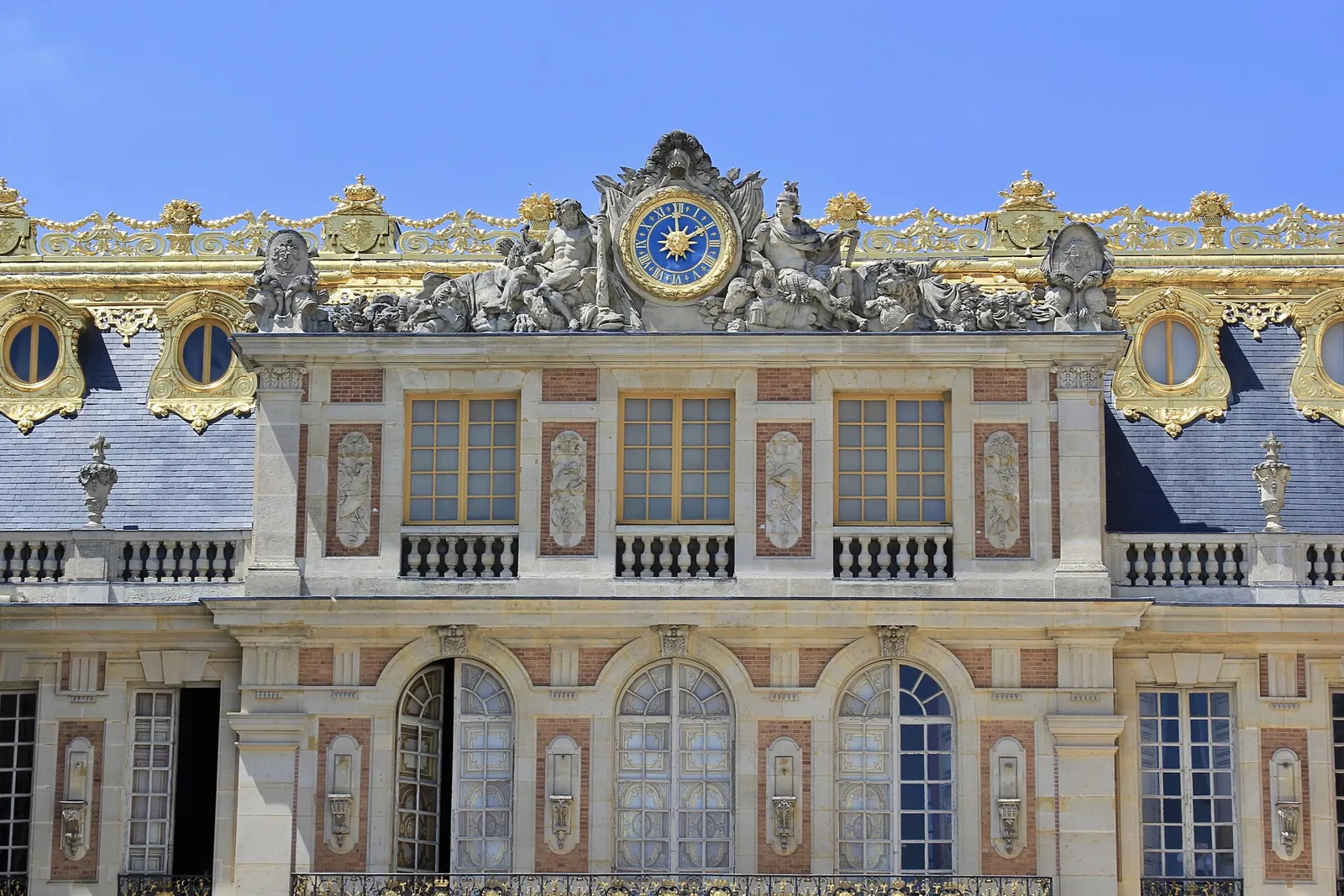 Brick and stone façade of the Marble Courtyard at the Palace of Versailles, with the great gilded clock and sculptures on the slate roof