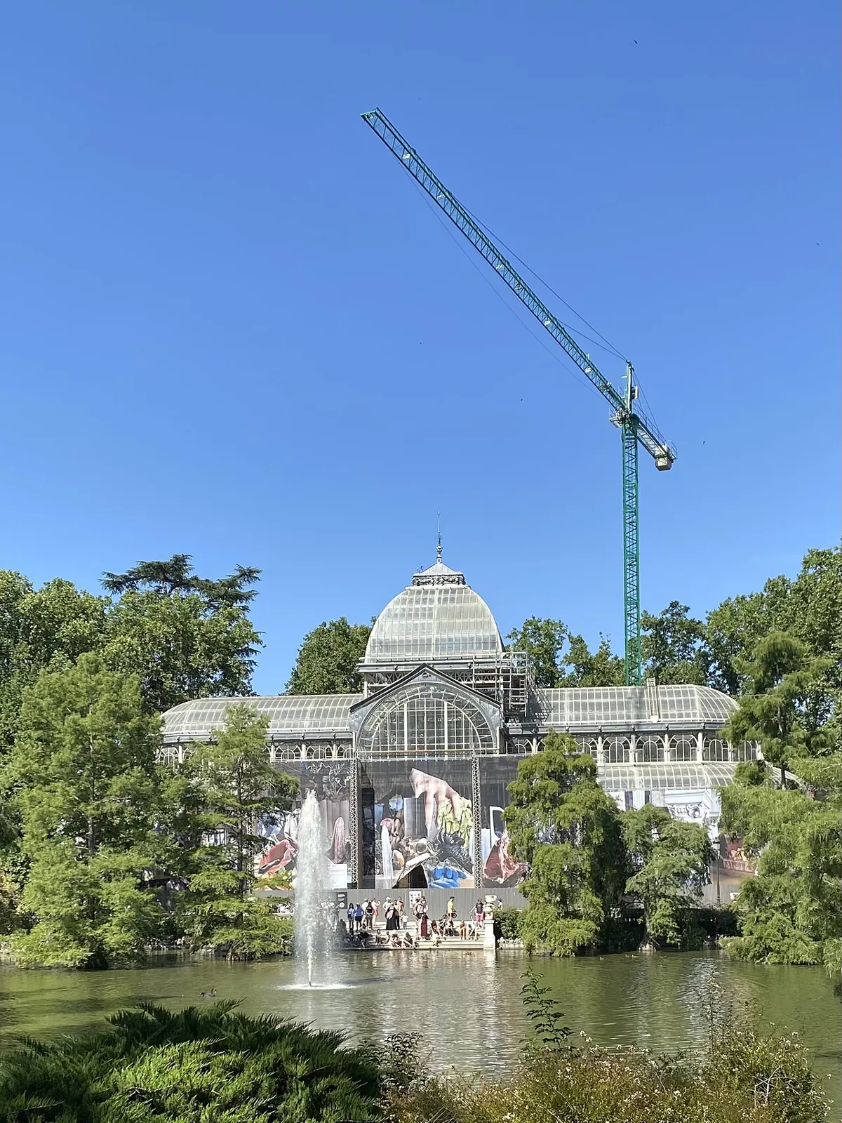 The Palacio de Cristal under restoration seen from the lake: a tall crane above the dome and the lower part covered by a printed canvas