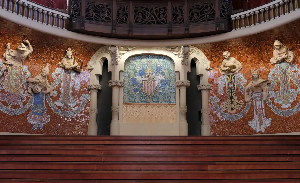 The back wall of the stage at the Palau de la Música Catalana: half-figures of muses emerging from a red mosaic, with a mosaic shield in the centre