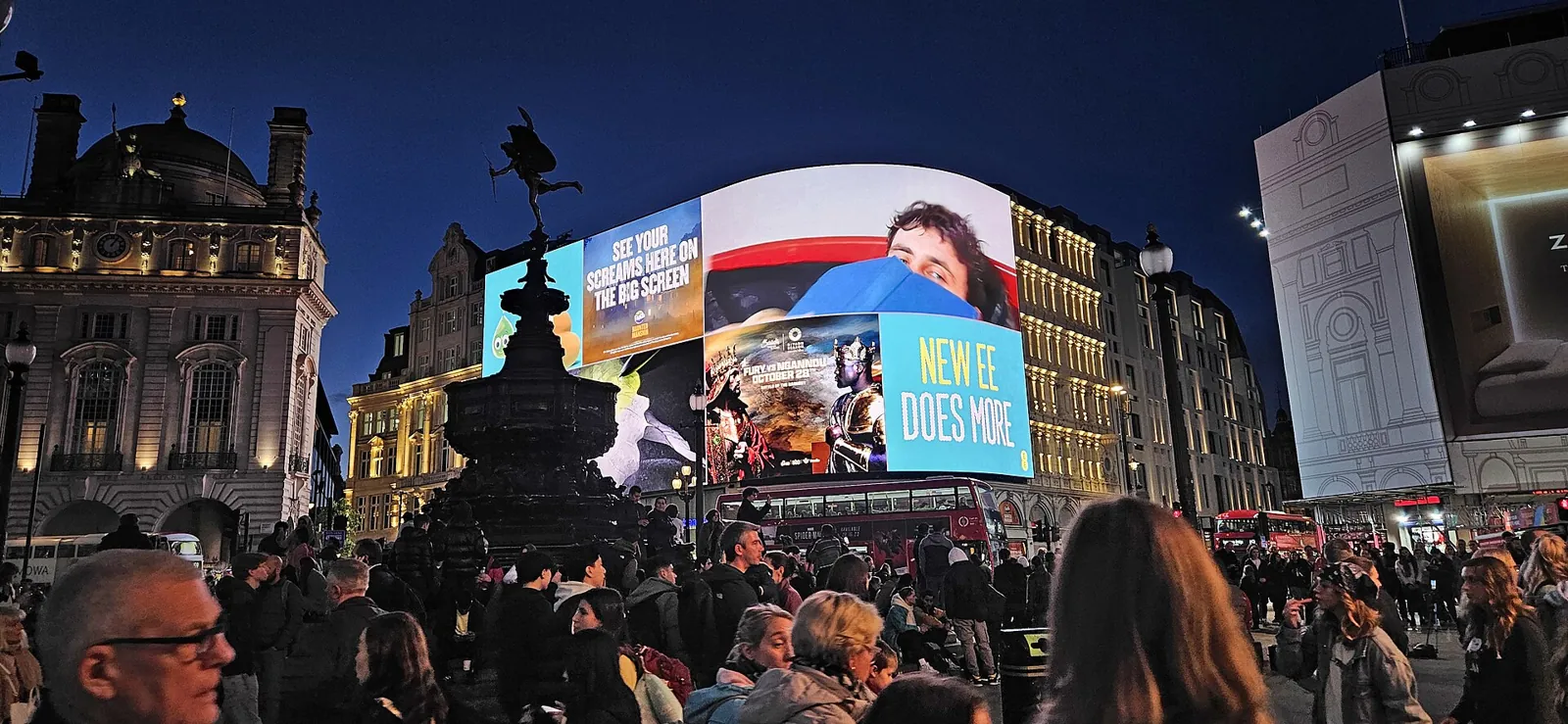 Piccadilly Circus at night, with the curved screen lit up, the fountain in silhouette and crowds in the square