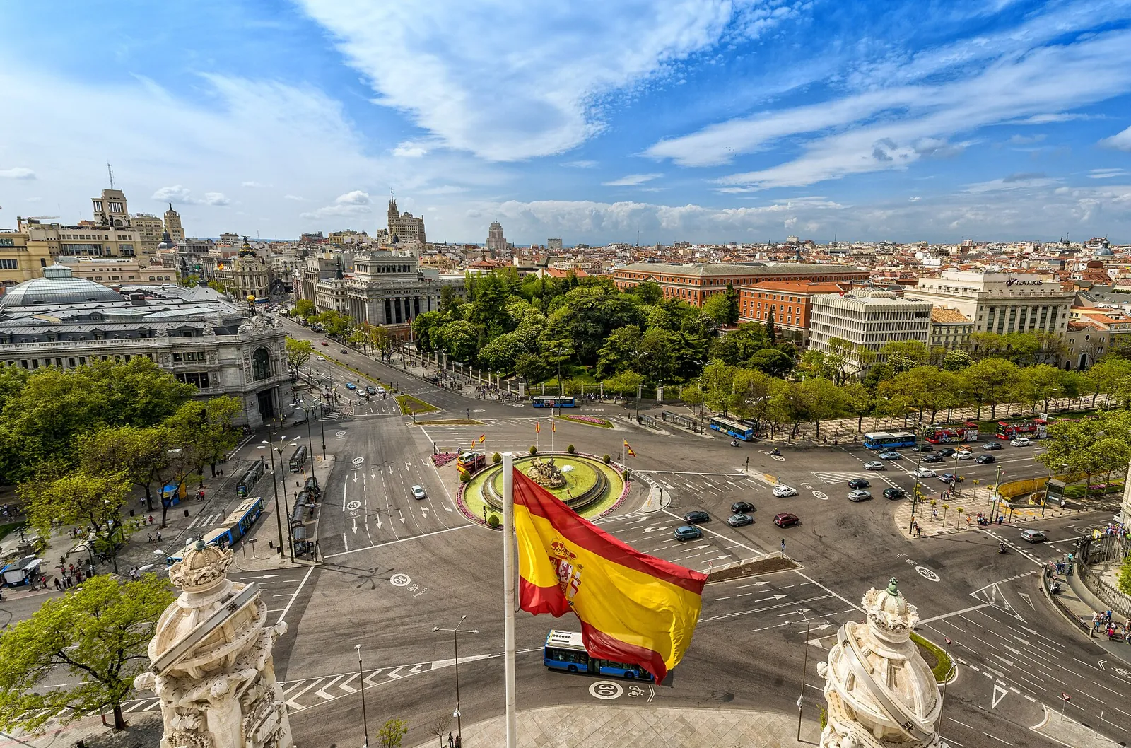 Plaza de Cibeles seen from the top of the Palacio de Cibeles: the roundabout with the fountain in the middle, traffic around it, a Spanish flag and Madrid's rooftops beyond