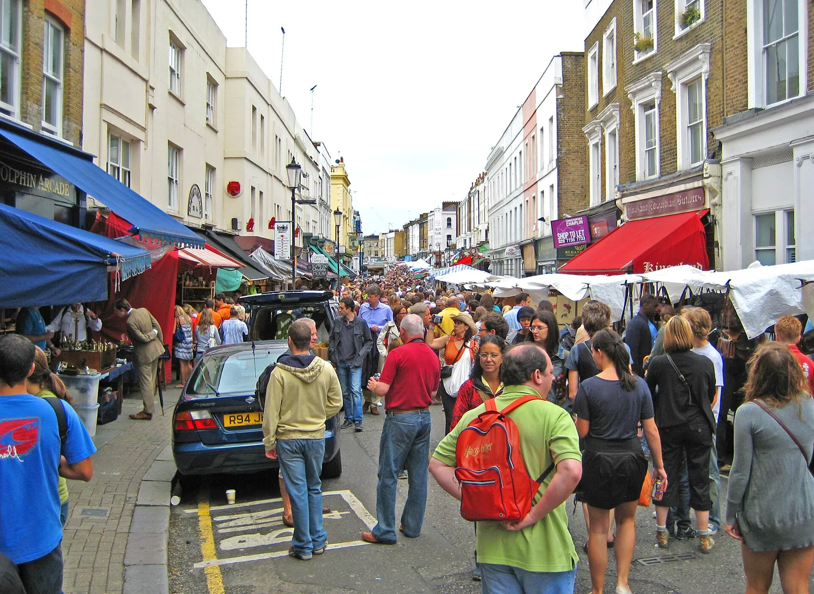 Portobello Road packed with people on a market day, with shop awnings and the white canopies of the stalls on both sides