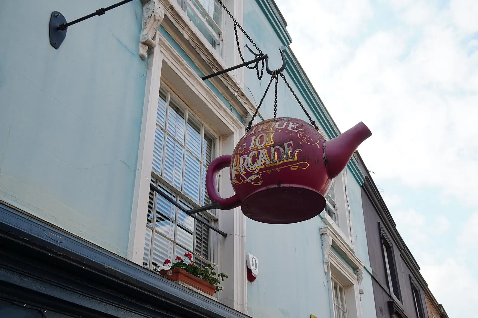 A giant red teapot hanging as a sign above the pale blue front of an antiques arcade on Portobello Road