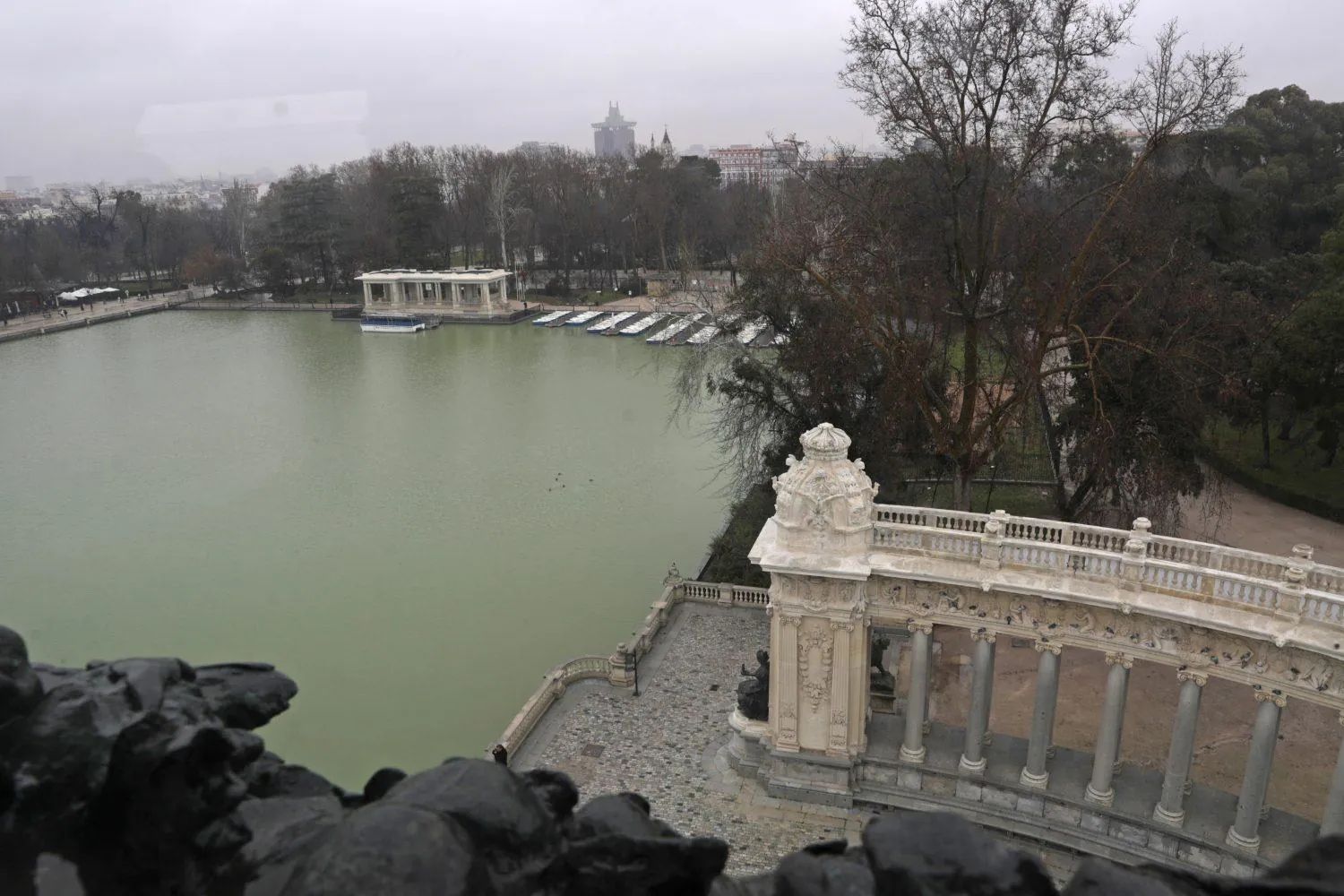 The Retiro boating lake seen from the top of the Alfonso XII monument, with bronze sculptures in the foreground and the boat dock across the water