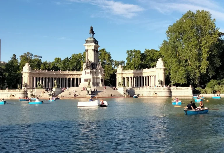 The Estanque Grande in Retiro Park with blue rowing boats and, behind it, the curved colonnade of the Alfonso XII monument topped by an equestrian statue