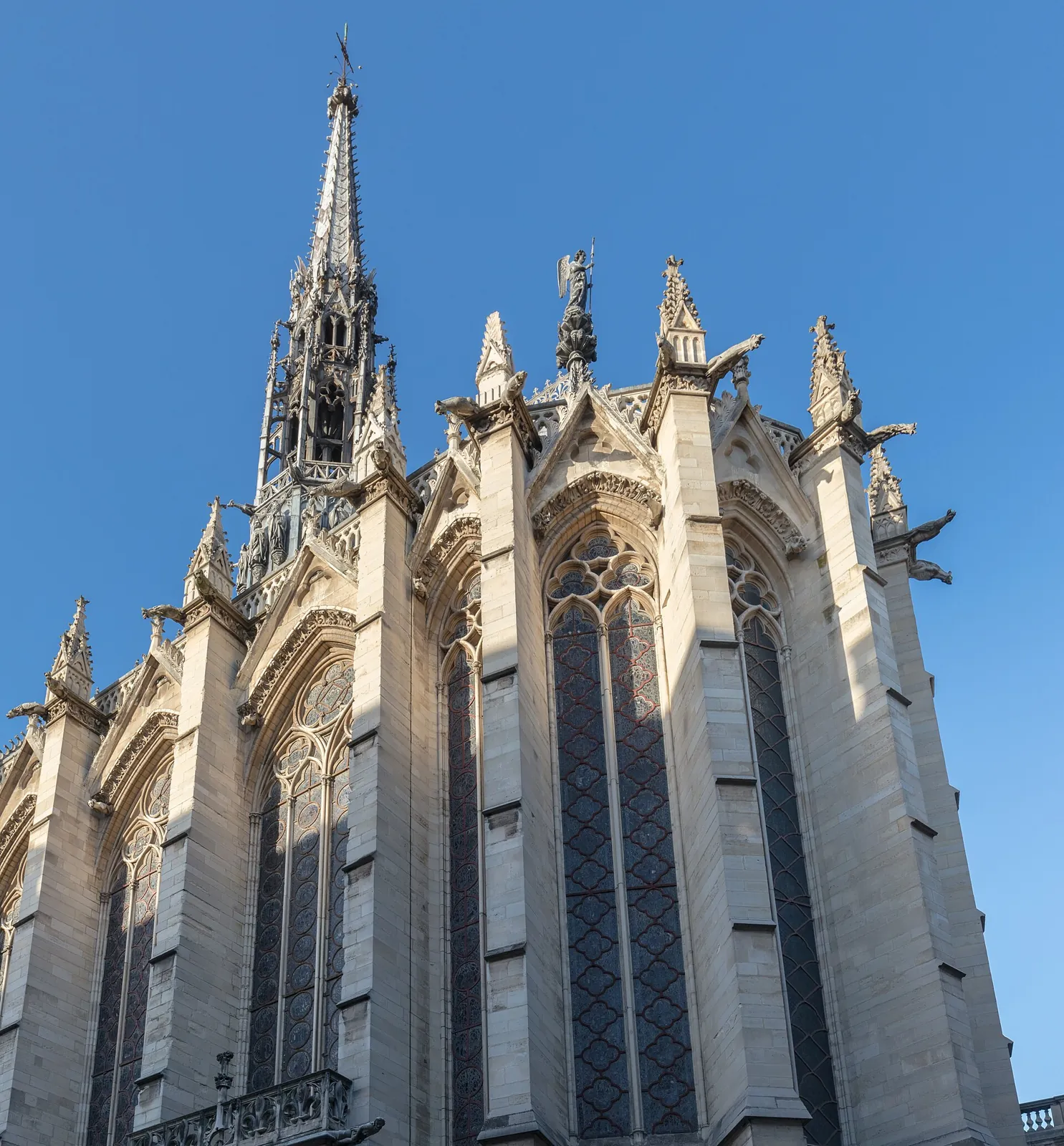 Gothic exterior of the Sainte-Chapelle seen from below, with its buttresses, gargoyles and the spire against a blue sky