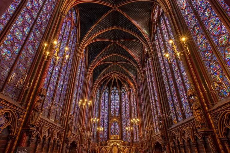 Inside the upper chapel of the Sainte-Chapelle: walls of blue and red stained glass up to the vault, gilded columns and the apse at the far end