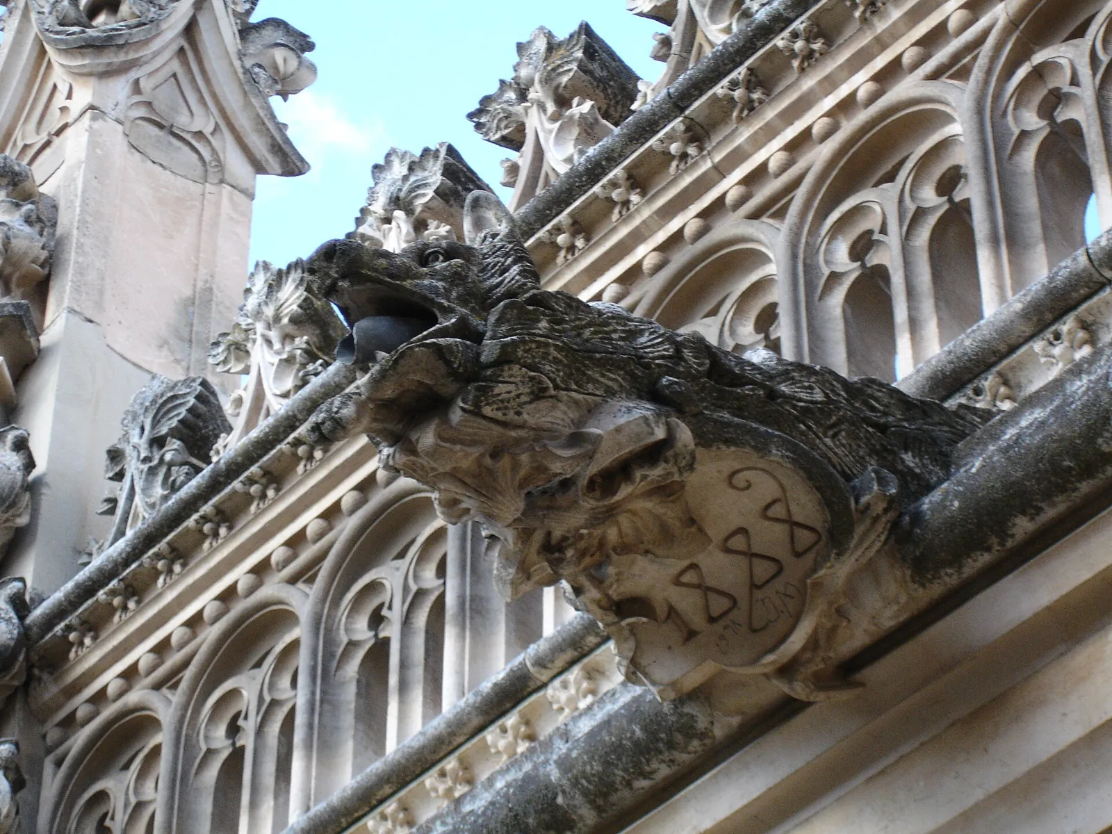 A stone gargoyle shaped like a wolf in the cloister of San Juan de los Reyes; the shield it holds bears the year 1888