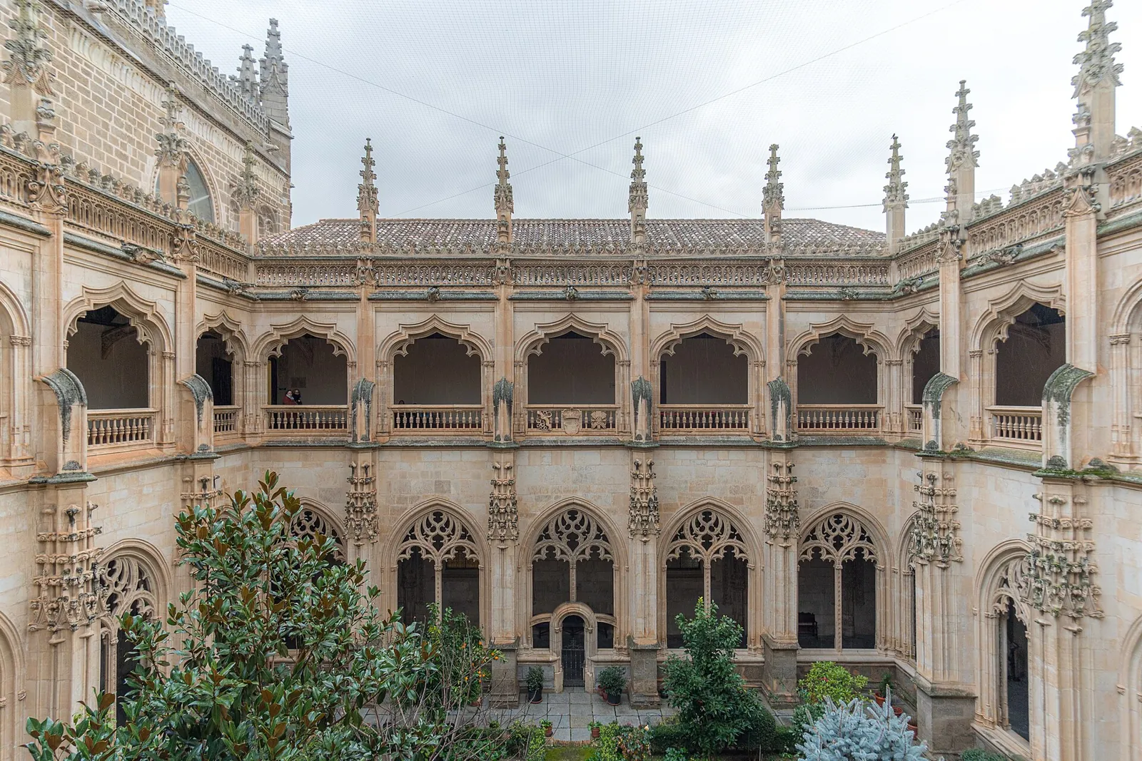 The cloister of San Juan de los Reyes seen from the garden, with its 2 storeys of Gothic arches, the openwork cresting and the pinnacles along the roof