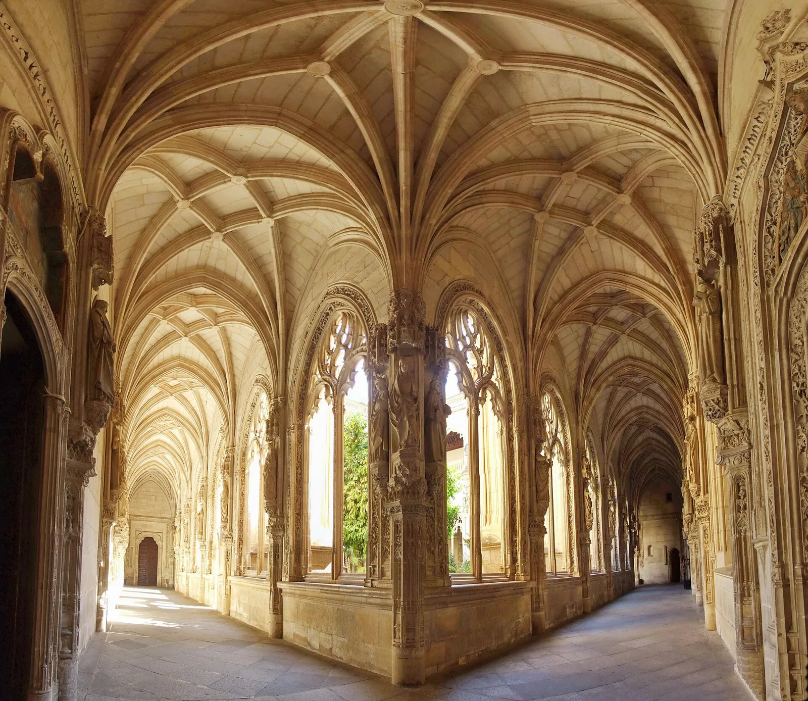 A walk of the lower cloister of San Juan de los Reyes, with rib vaults and pierced Gothic windows opening onto the garden