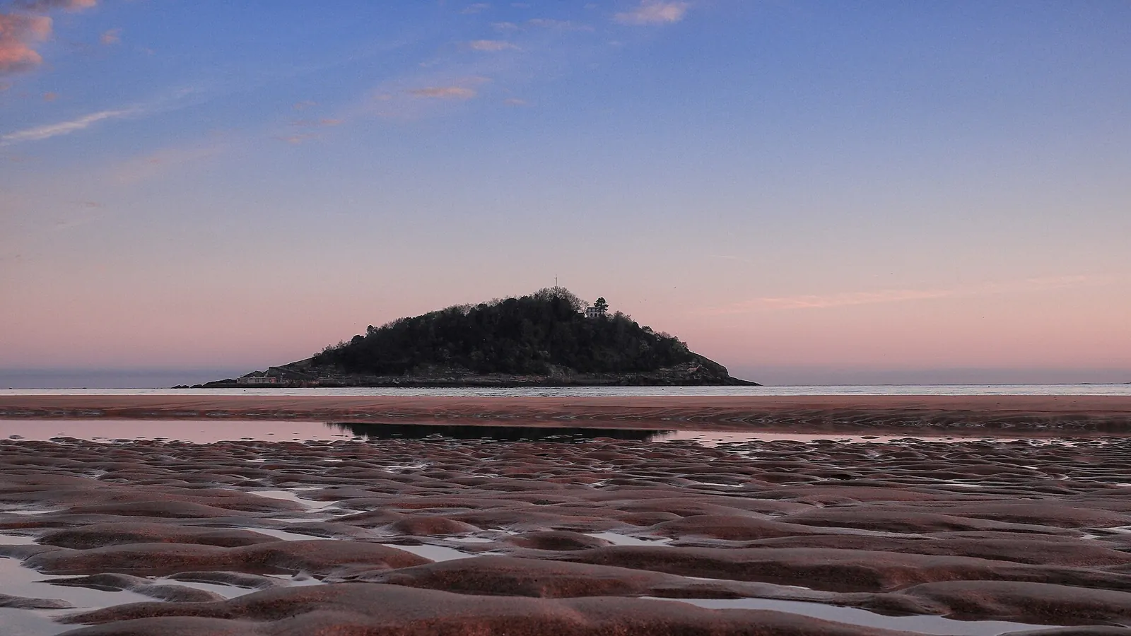 Santa Clara Island at dawn seen from La Concha beach, with wet, rippled sand in the foreground