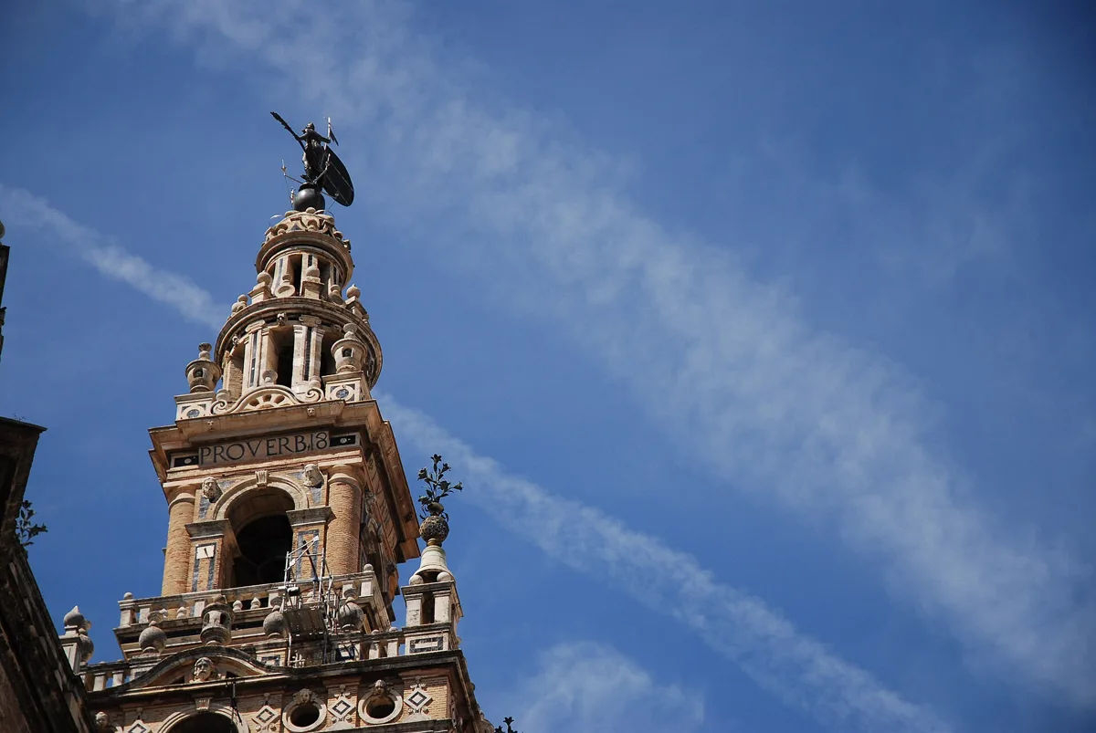 The Renaissance top of the Giralda against a blue sky: the band with the Latin inscription, the round upper body and the Giraldillo weather vane
